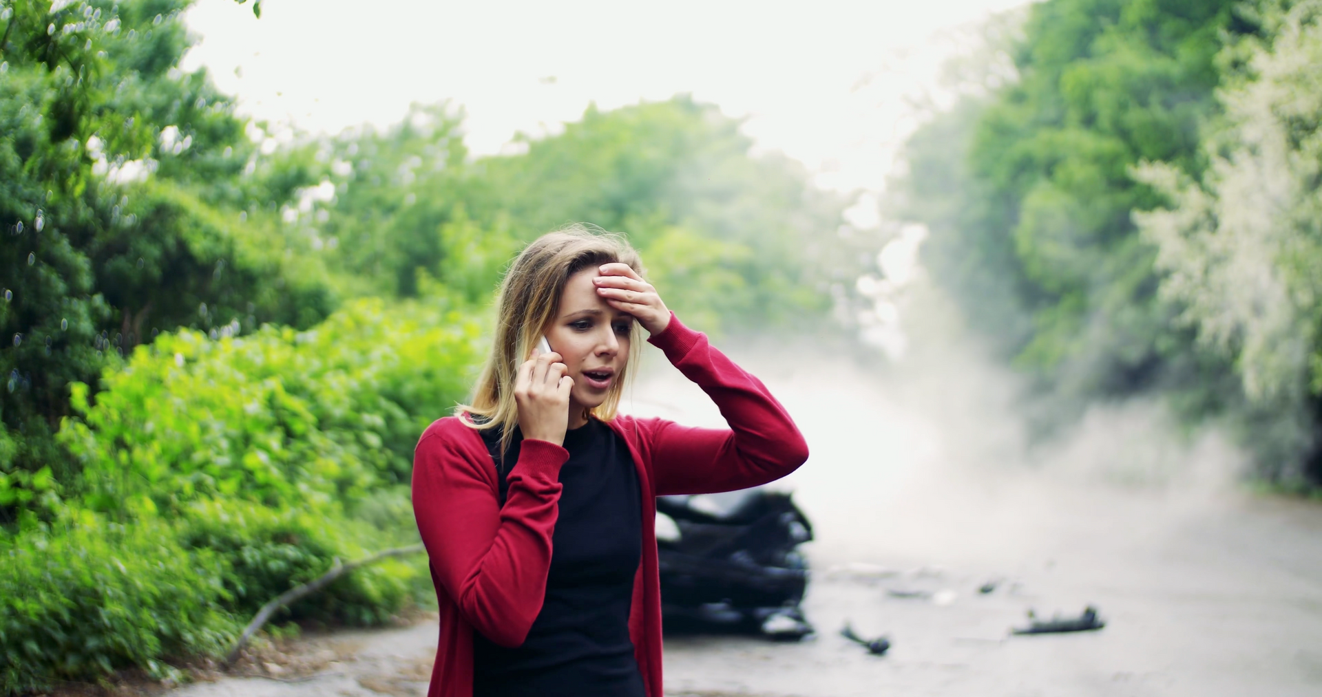 A woman is talking on a cell phone in front of a car accident.