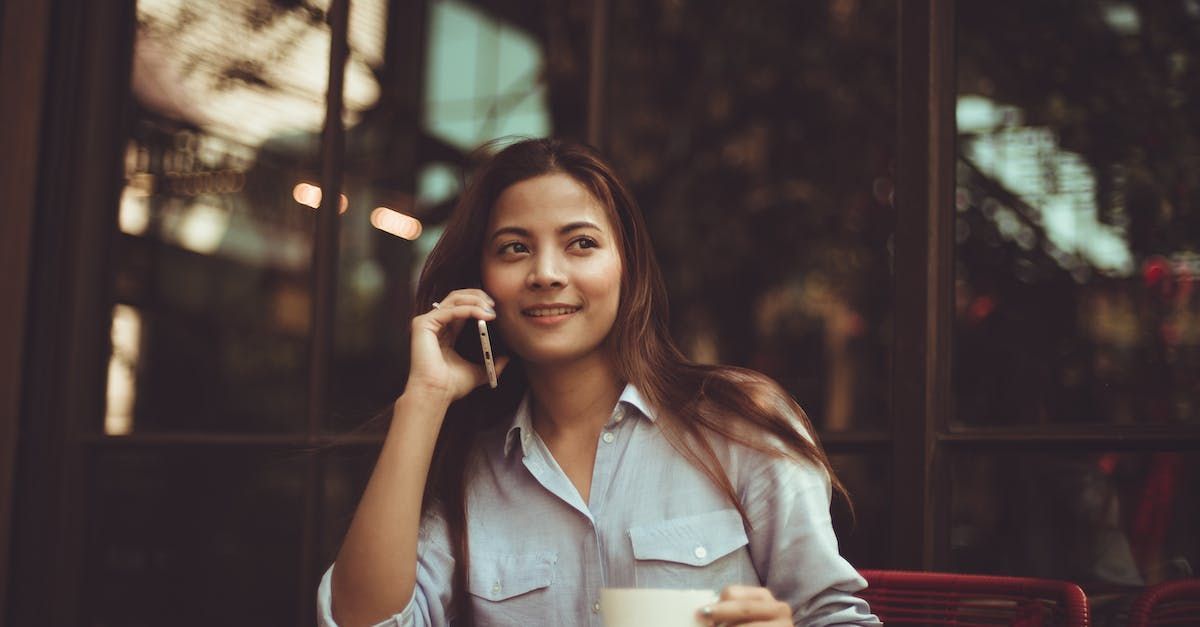 A woman is sitting at a table talking on a cell phone while holding a cup of milk.