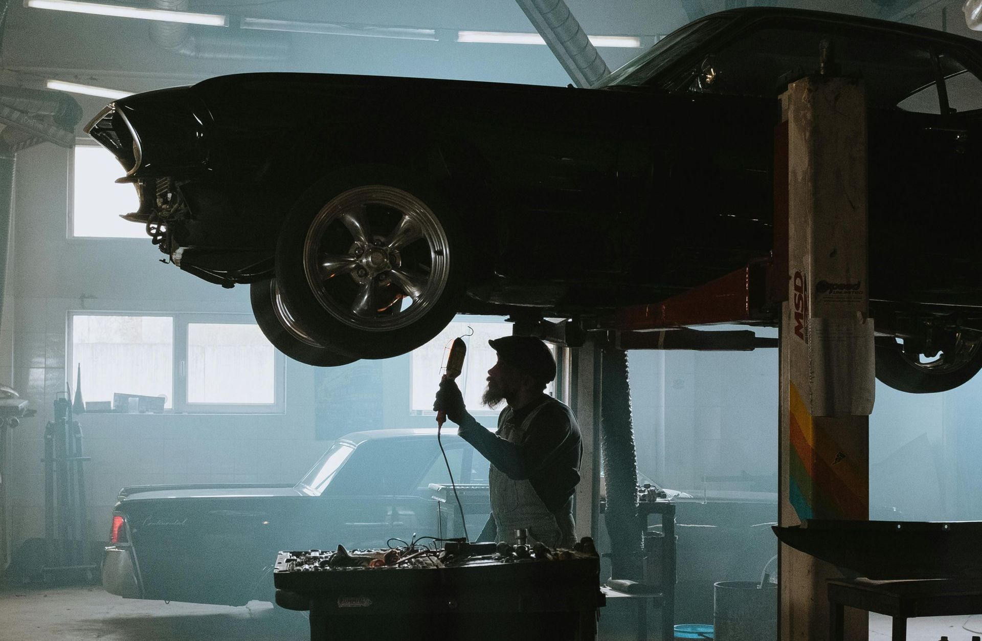 A man is working on a car on a lift in a garage.