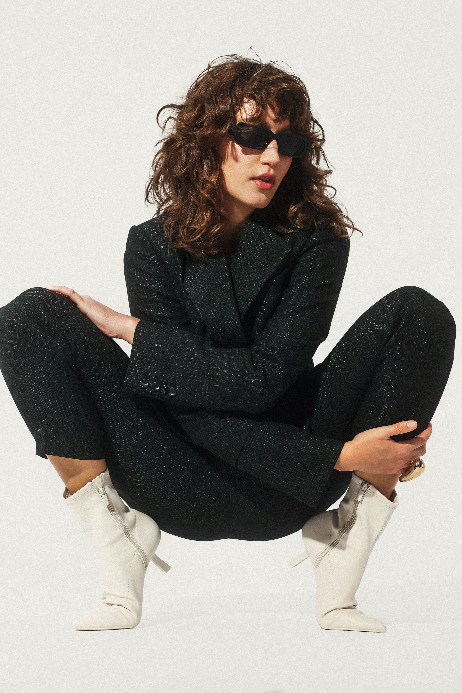 Kobieta kuca w okularach przeciwsłonecznych i białych butach