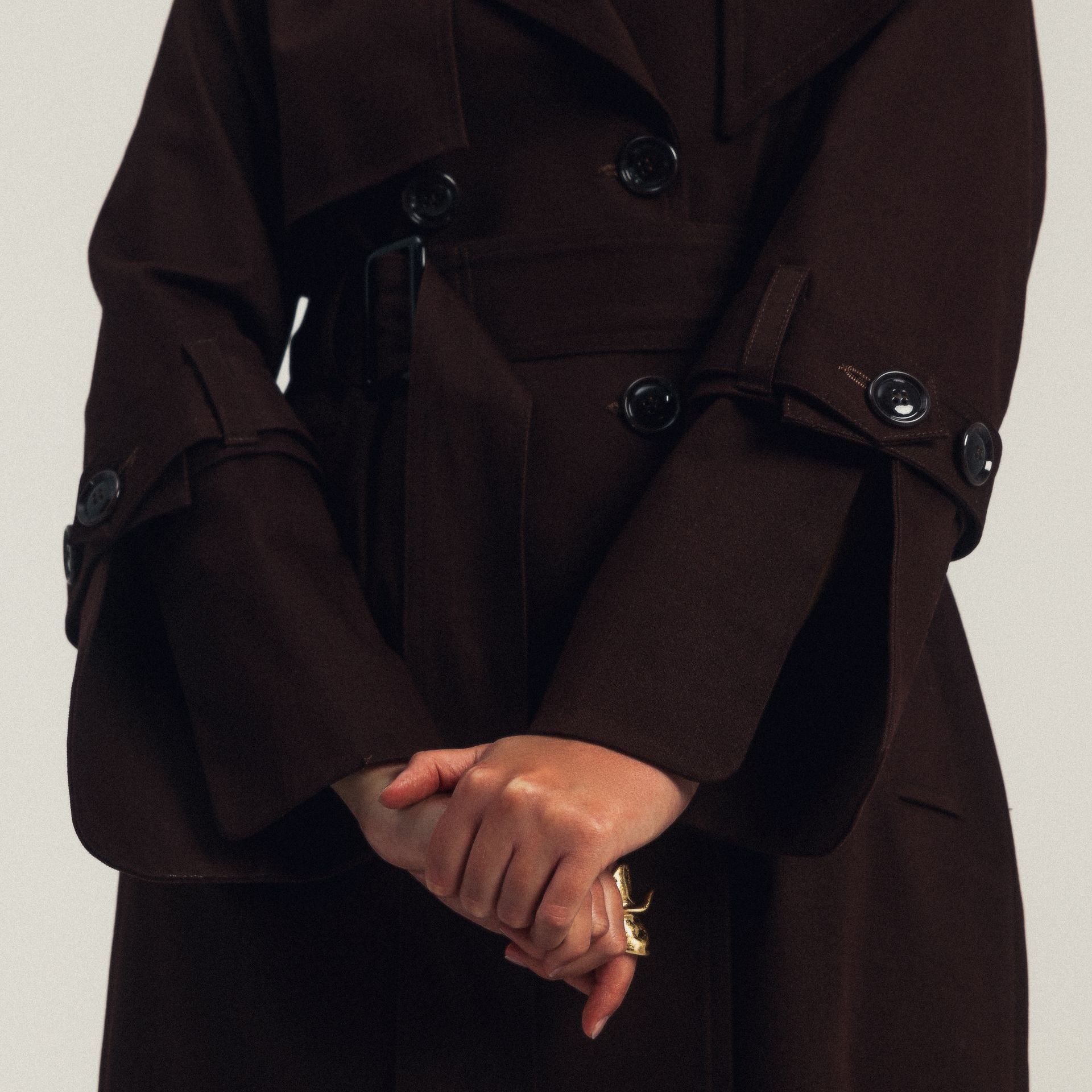 Kobieta w brązowym płaszczu trzyma ręce razem