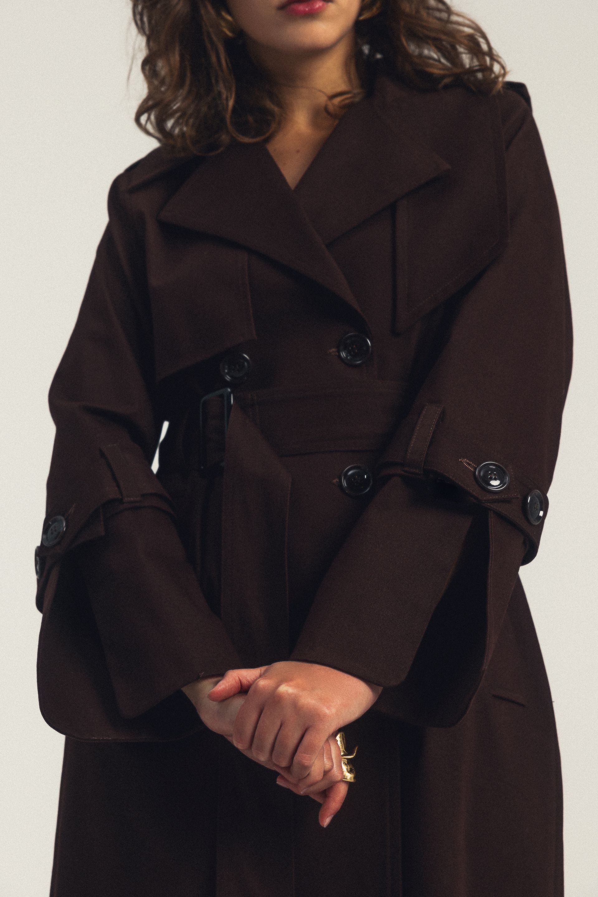 Kobieta ubrana w brązowy trencz z guzikami na rękawach