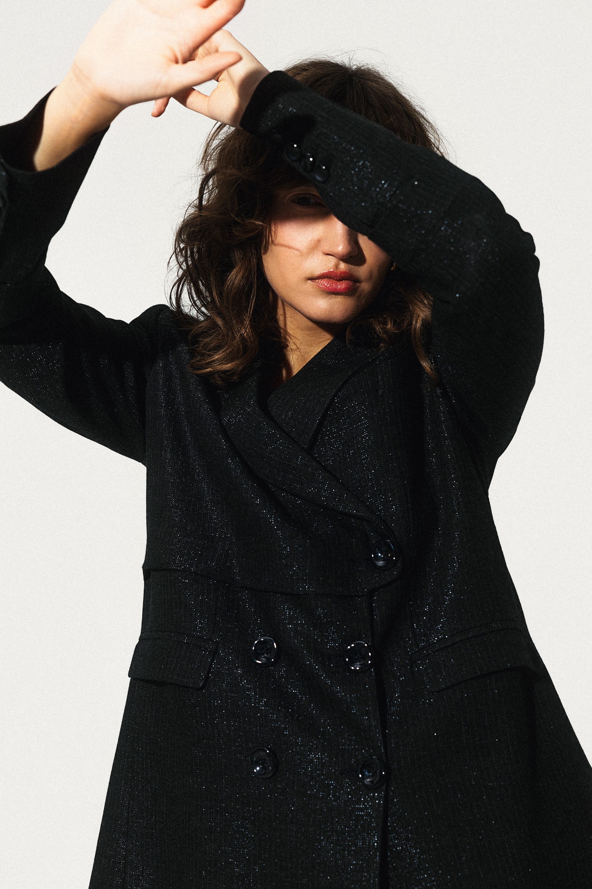 Kobieta w czarnym płaszczu zasłaniająca twarz dłońmi