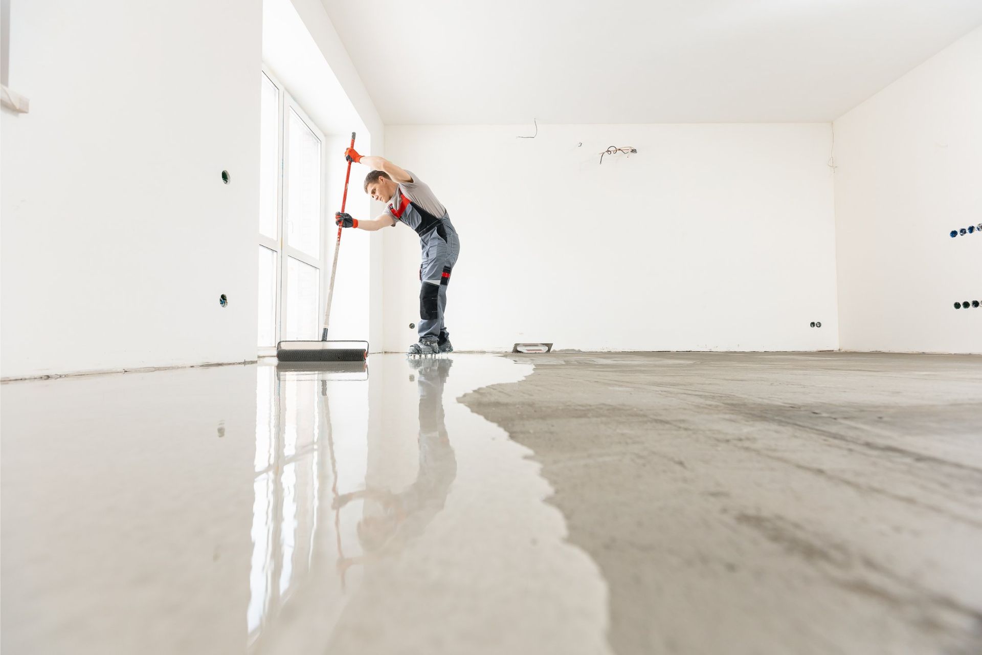Worker smoothing wet concrete floor with a squeegee in a new construction room.