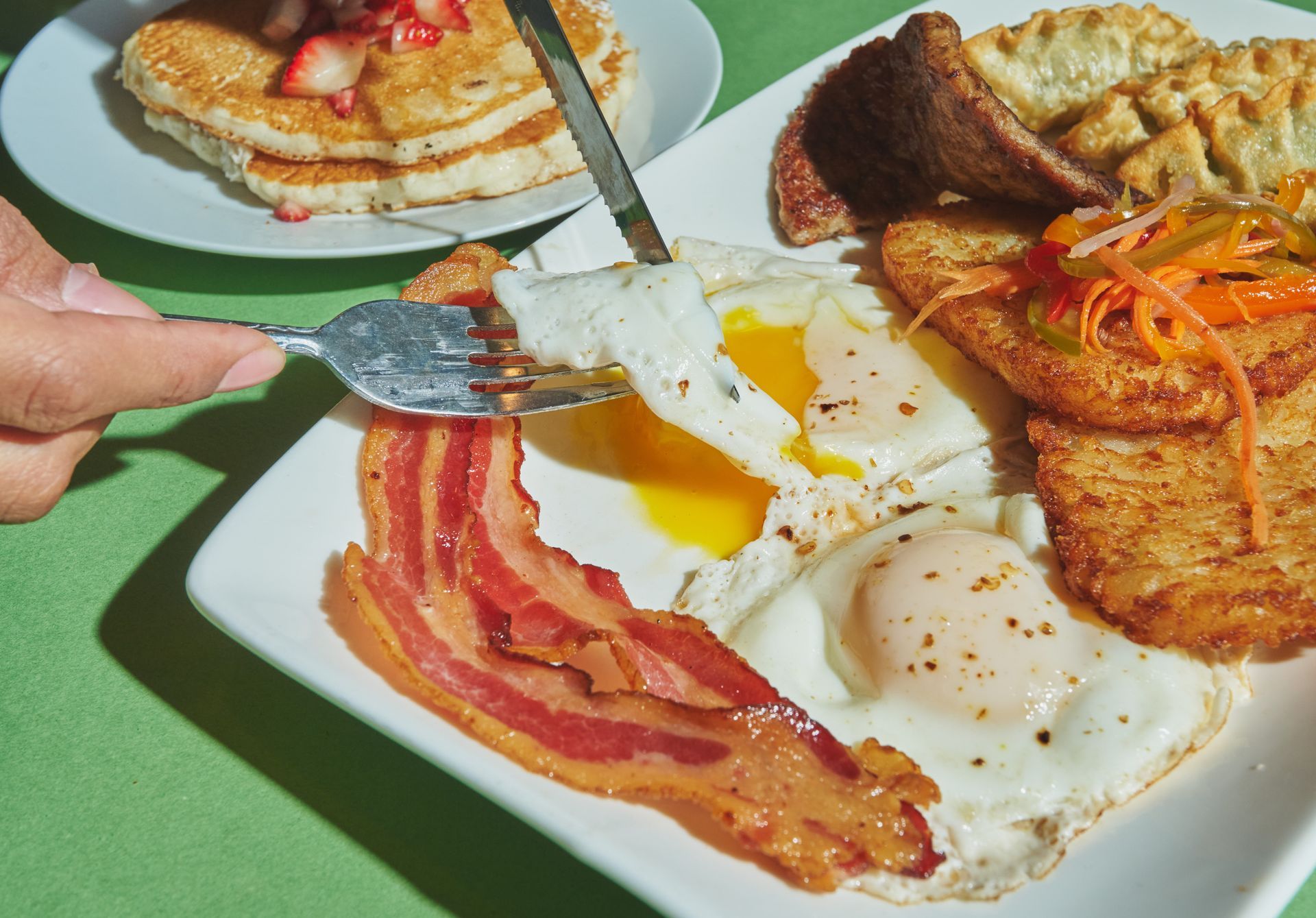 Breakfast plate with eggs, bacon, hash browns, and pancakes with strawberry topping.