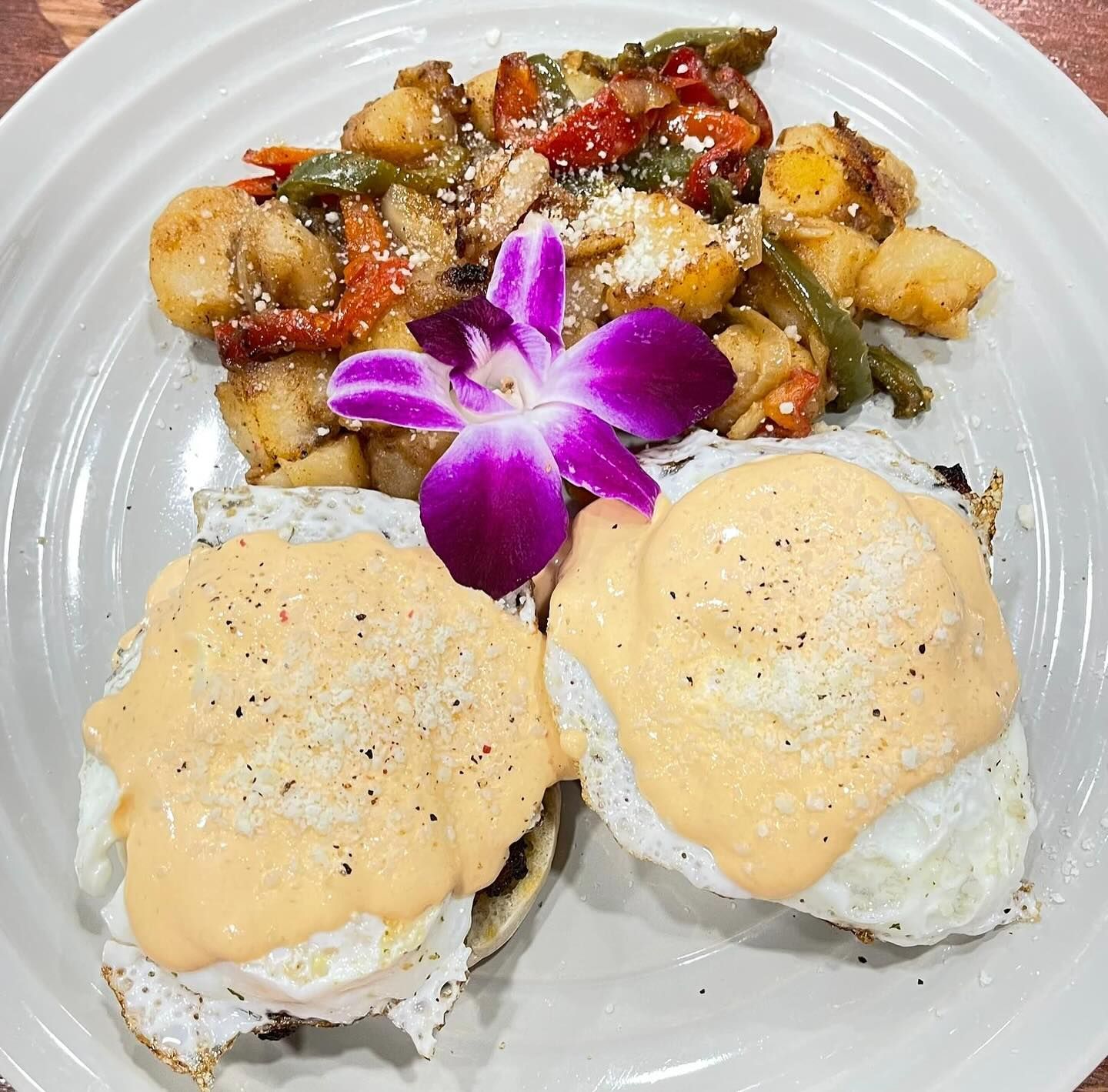 Eggs Benedict with potatoes and vegetables, garnished with a purple orchid.