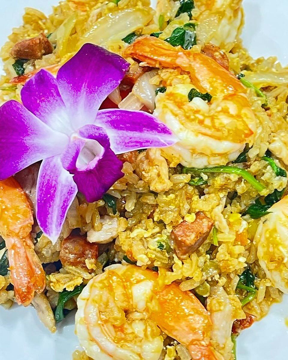 Shrimp fried rice with a purple orchid garnish. Close up with visible shrimp, rice, and vegetables.