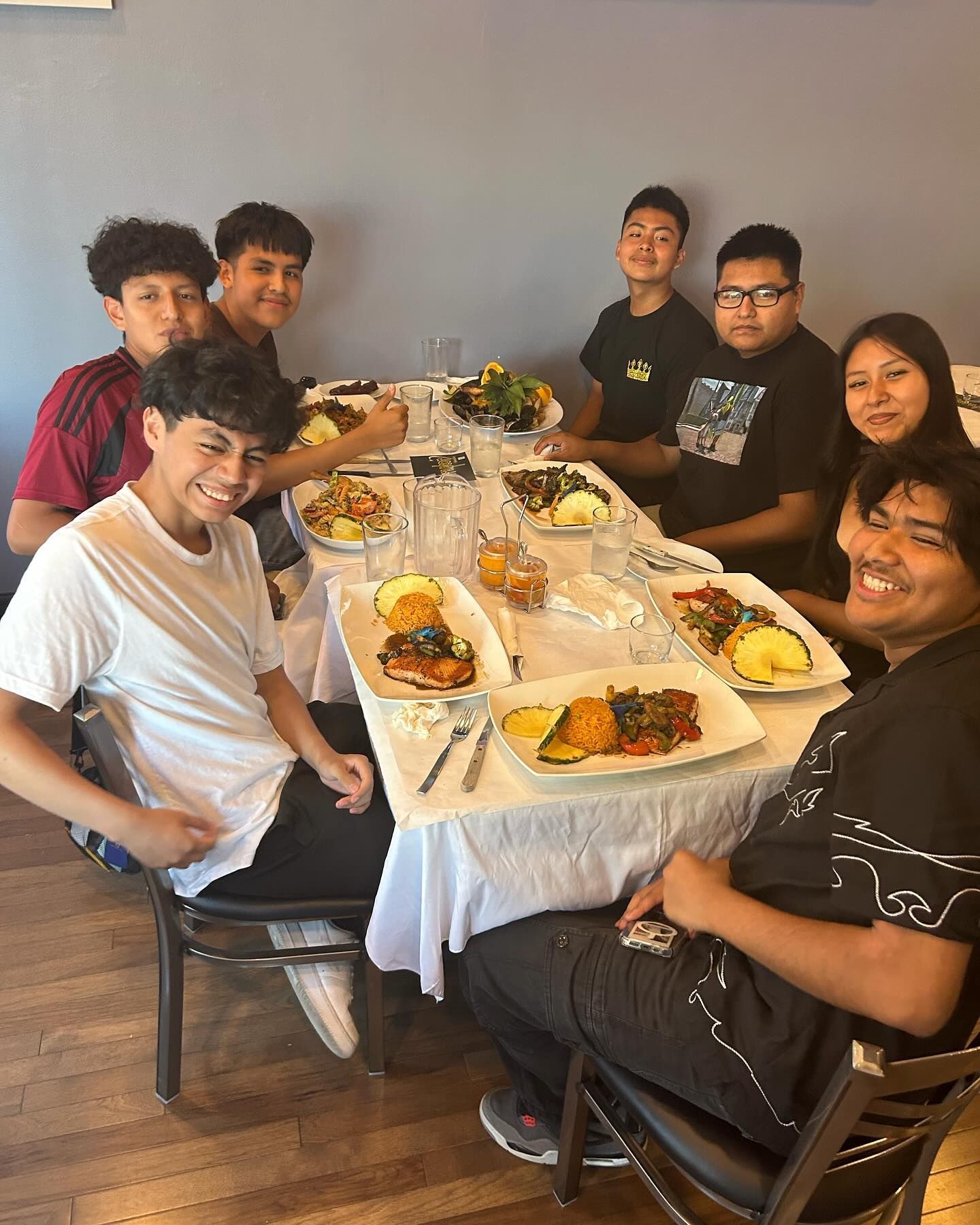 Group of people smiling around a table with food, in a restaurant setting.