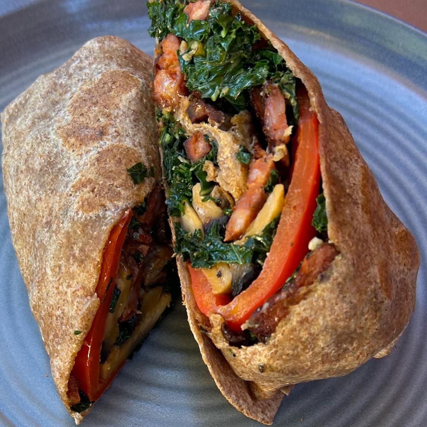 A wrap sandwich cut in half, filled with kale, red peppers, and what appears to be cheese, on a blue plate.