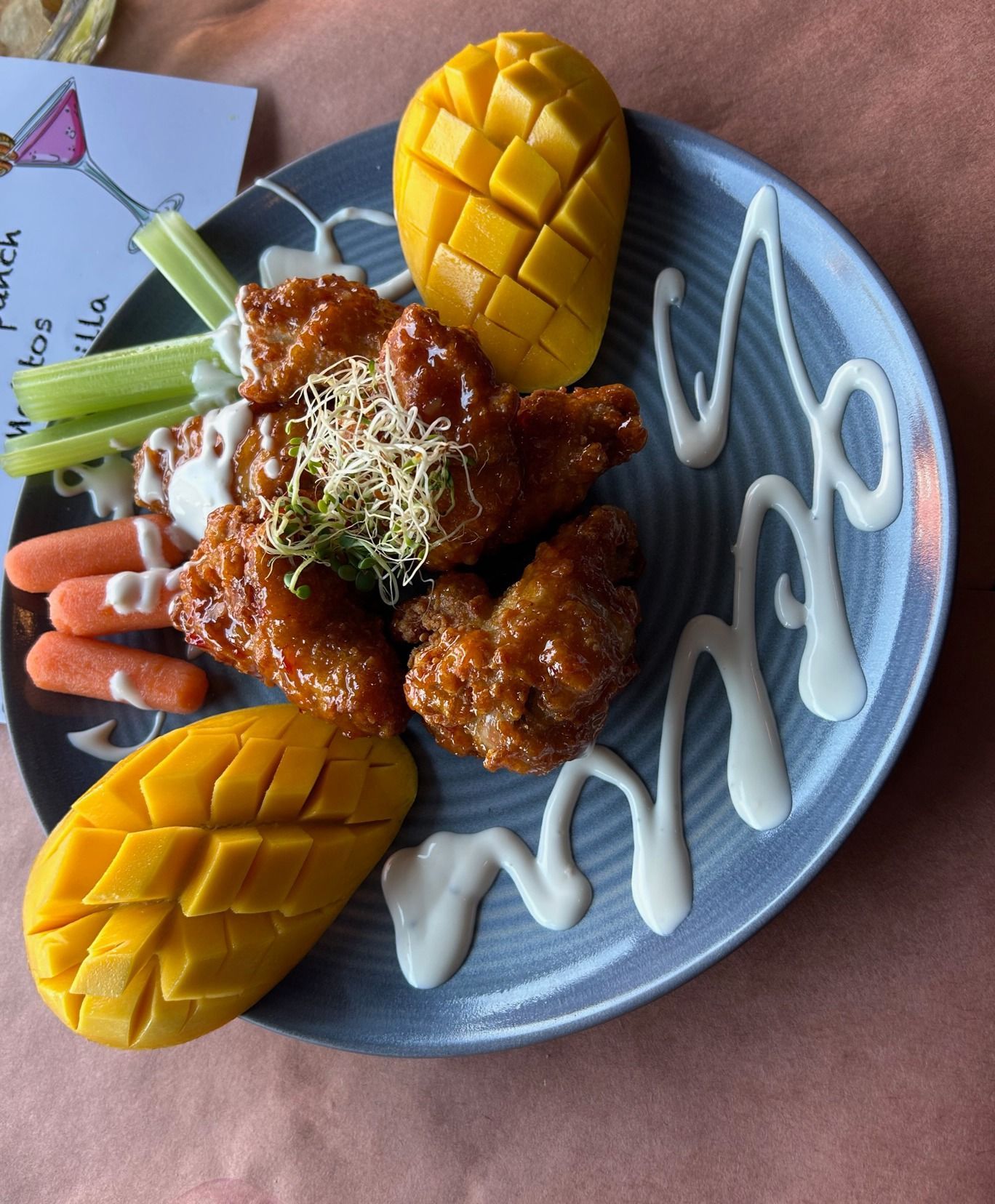 Chicken wings with mango, carrots, and celery on a plate, drizzled with white sauce.