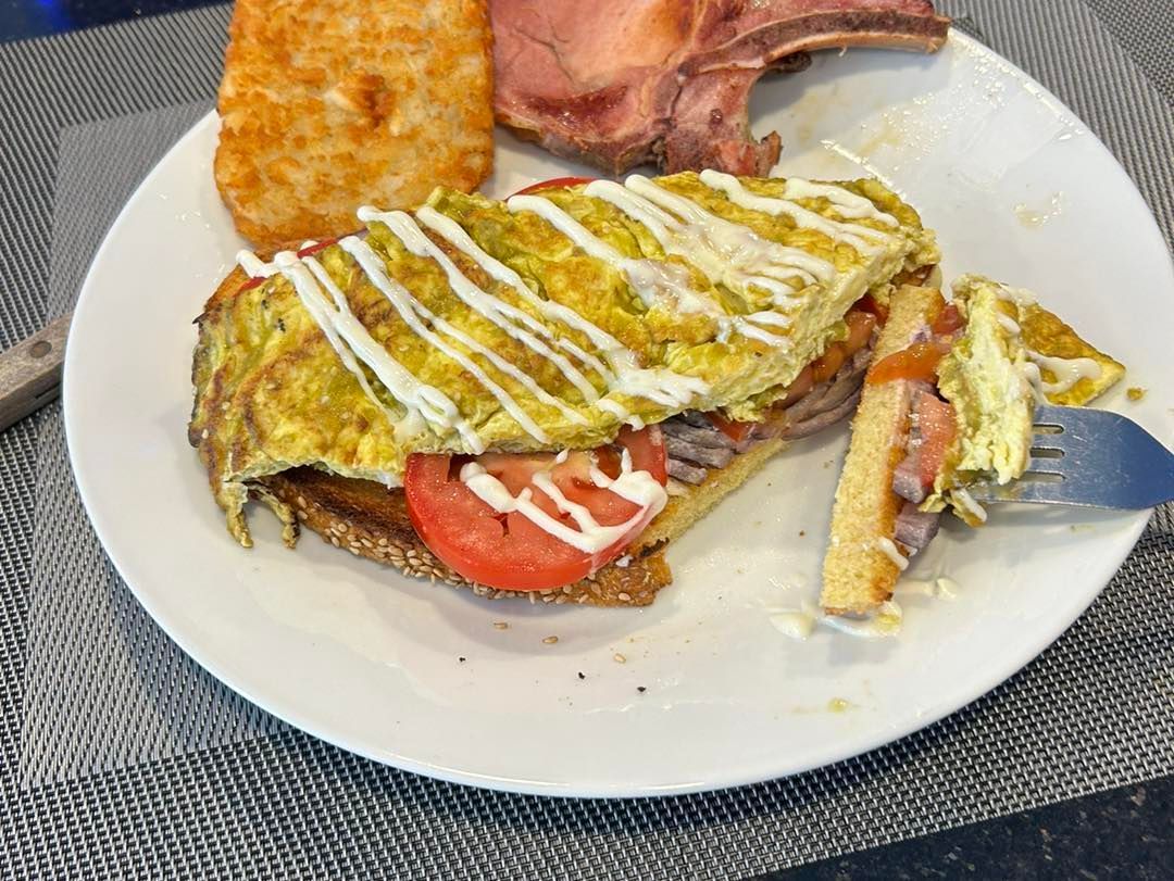 Plate with a sandwich, hash brown, and pork chop. Sandwich has egg, tomato, and sauce.