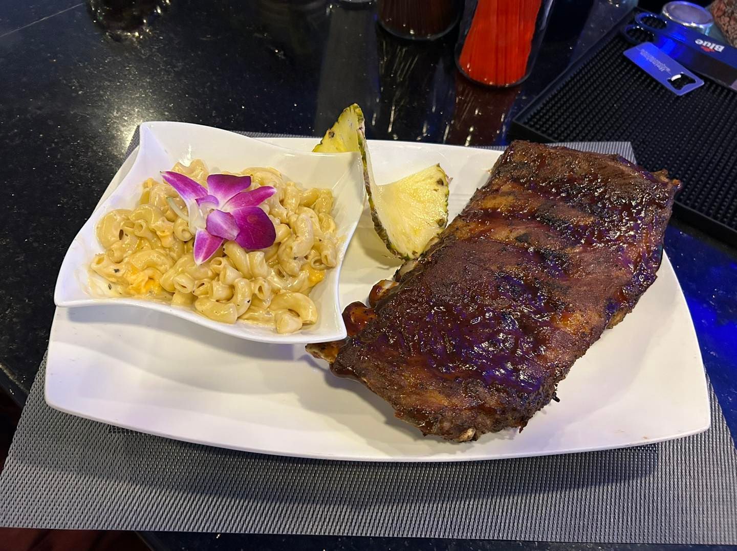 Plate with ribs, mac and cheese, pineapple, purple flower garnish.