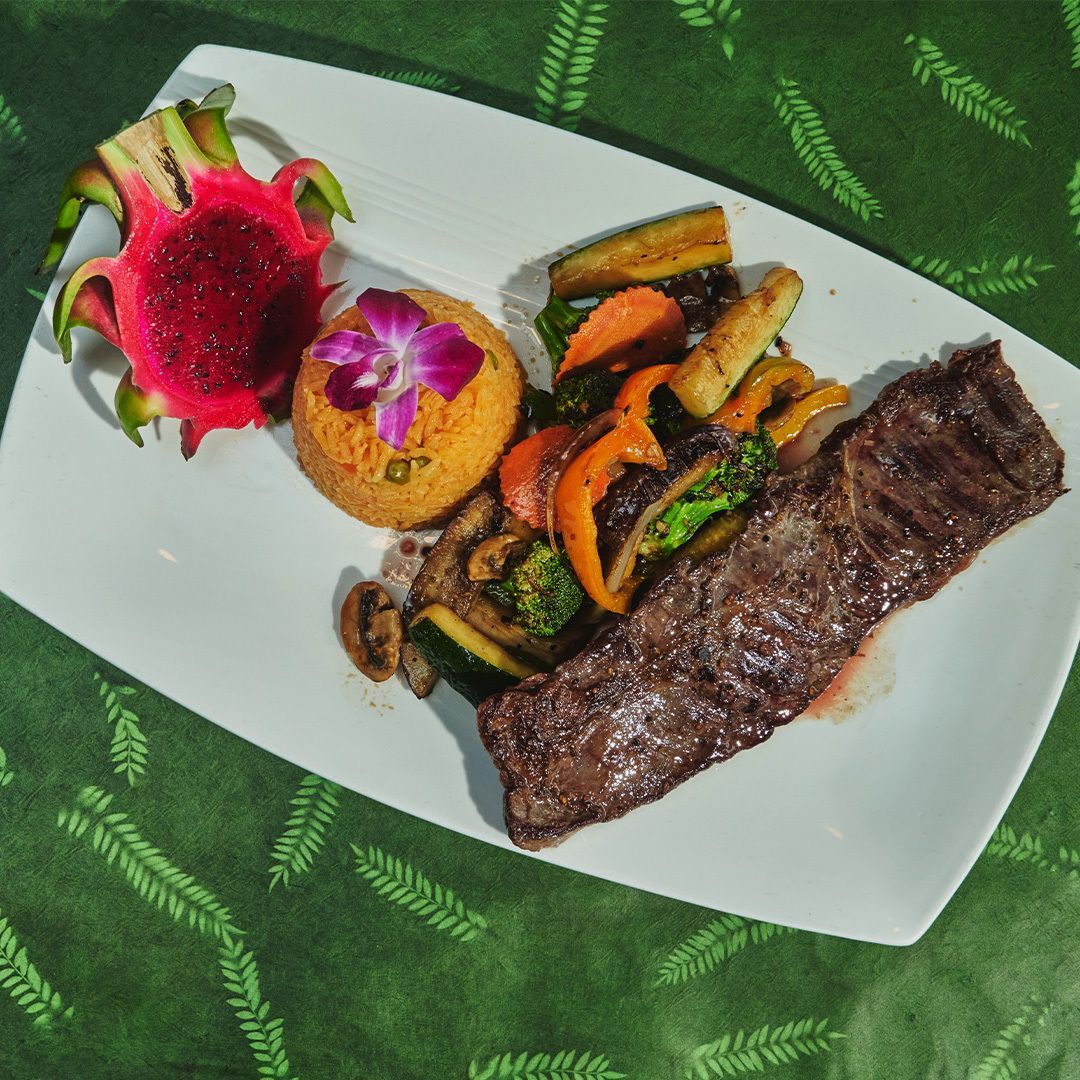 Grilled steak, rice, and roasted vegetables on a white plate with a dragon fruit garnish.