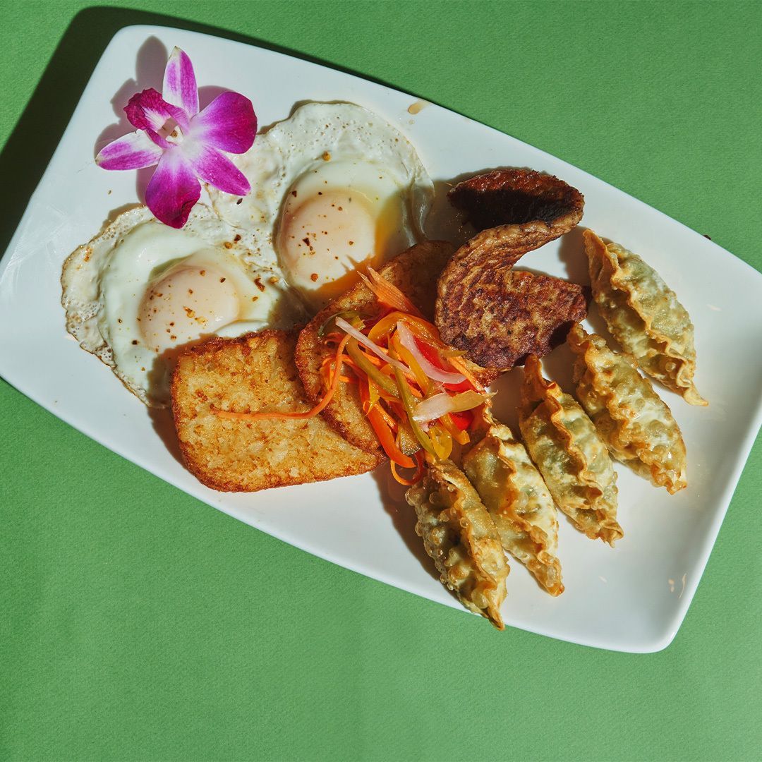 Plate of food with fried eggs, hash brown, dumplings, fried pork, and pickled vegetables, with orchid.