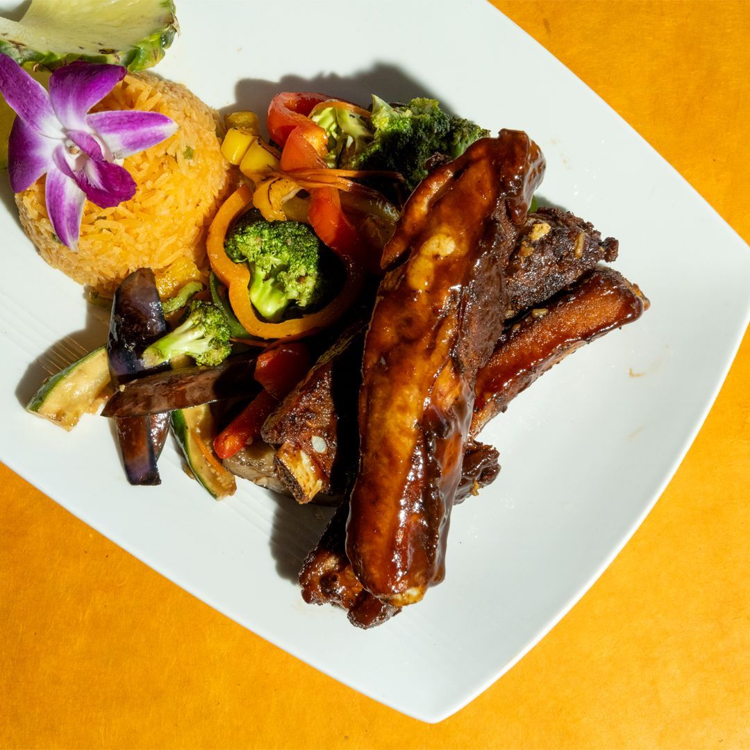 Plate of glazed ribs with colorful vegetables and rice.