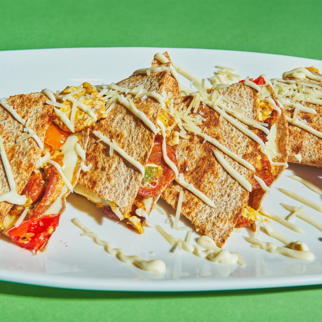 Grilled sandwich wedges on a white plate, drizzled with white sauce, against a green background.