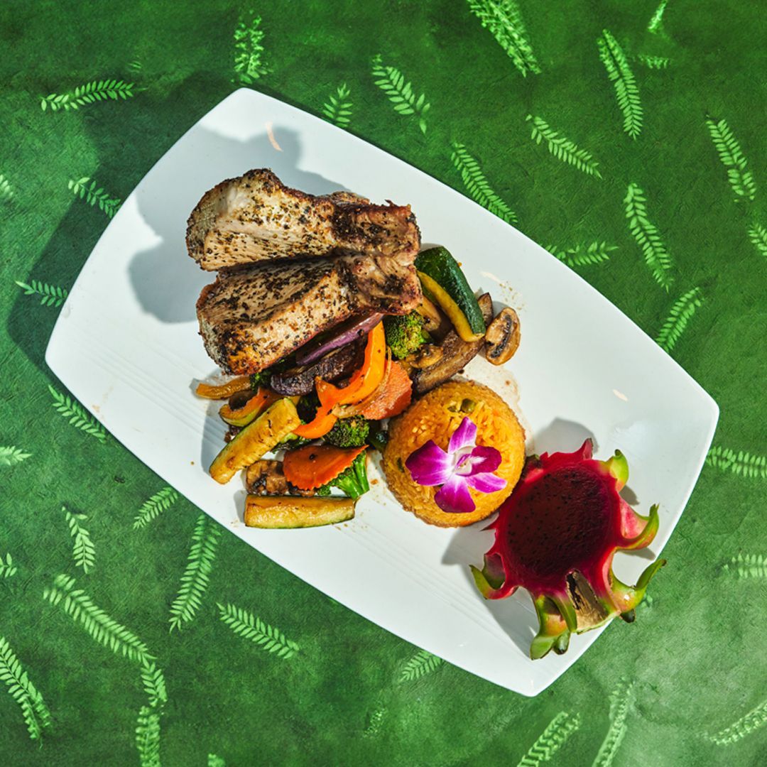 Grilled chicken with colorful roasted vegetables, rice, and dragon fruit on a white plate.