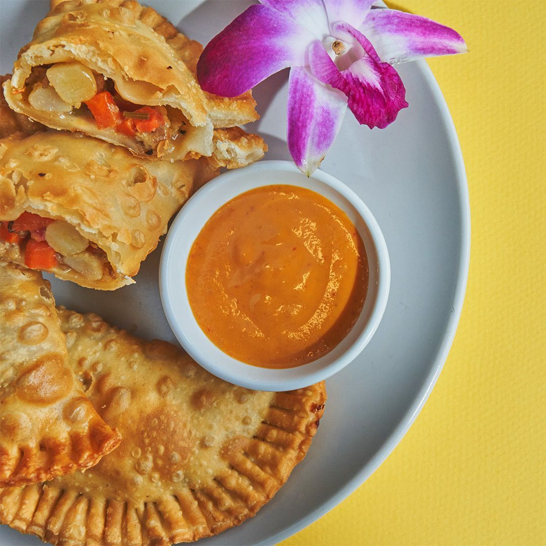 Empanadas with dipping sauce and orchid on a plate against yellow backdrop.