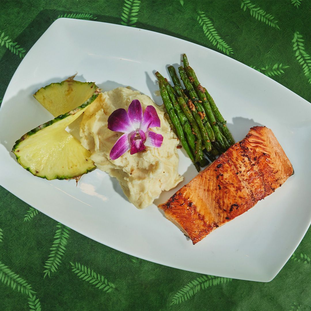 Grilled salmon with mashed potatoes, asparagus, and pineapple on a white plate.