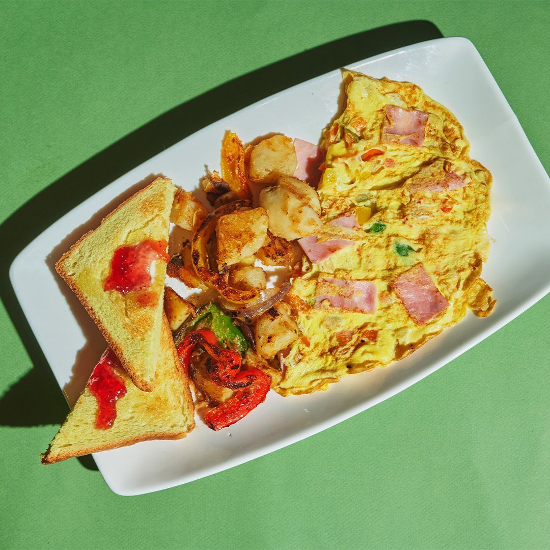 Breakfast plate: omelet with ham, toast with jelly, and potatoes on a green surface.