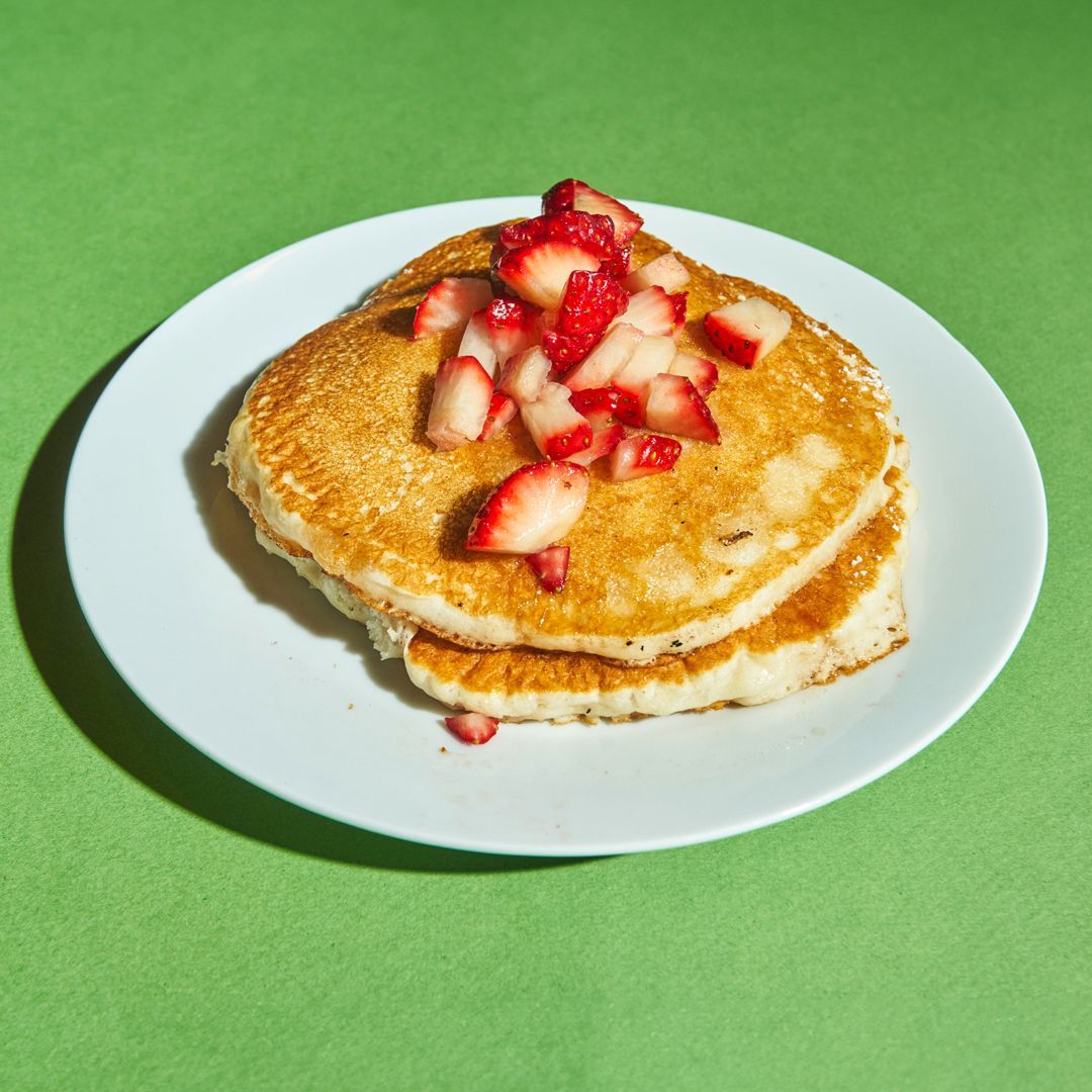 Pancakes topped with chopped strawberries on a white plate, against a green background.