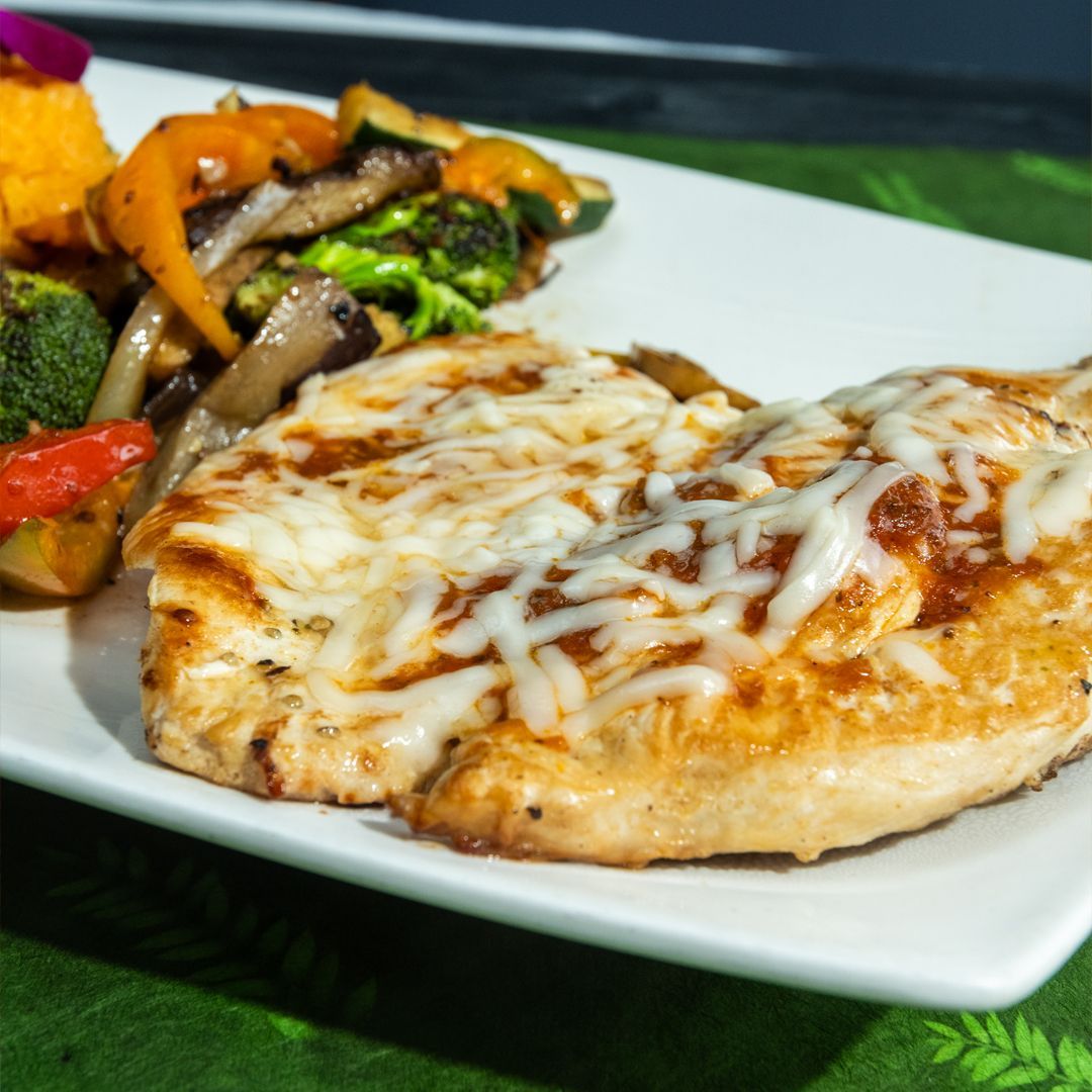 Grilled chicken breasts with melted cheese, sauteed vegetables, and sweet potato on a white plate.