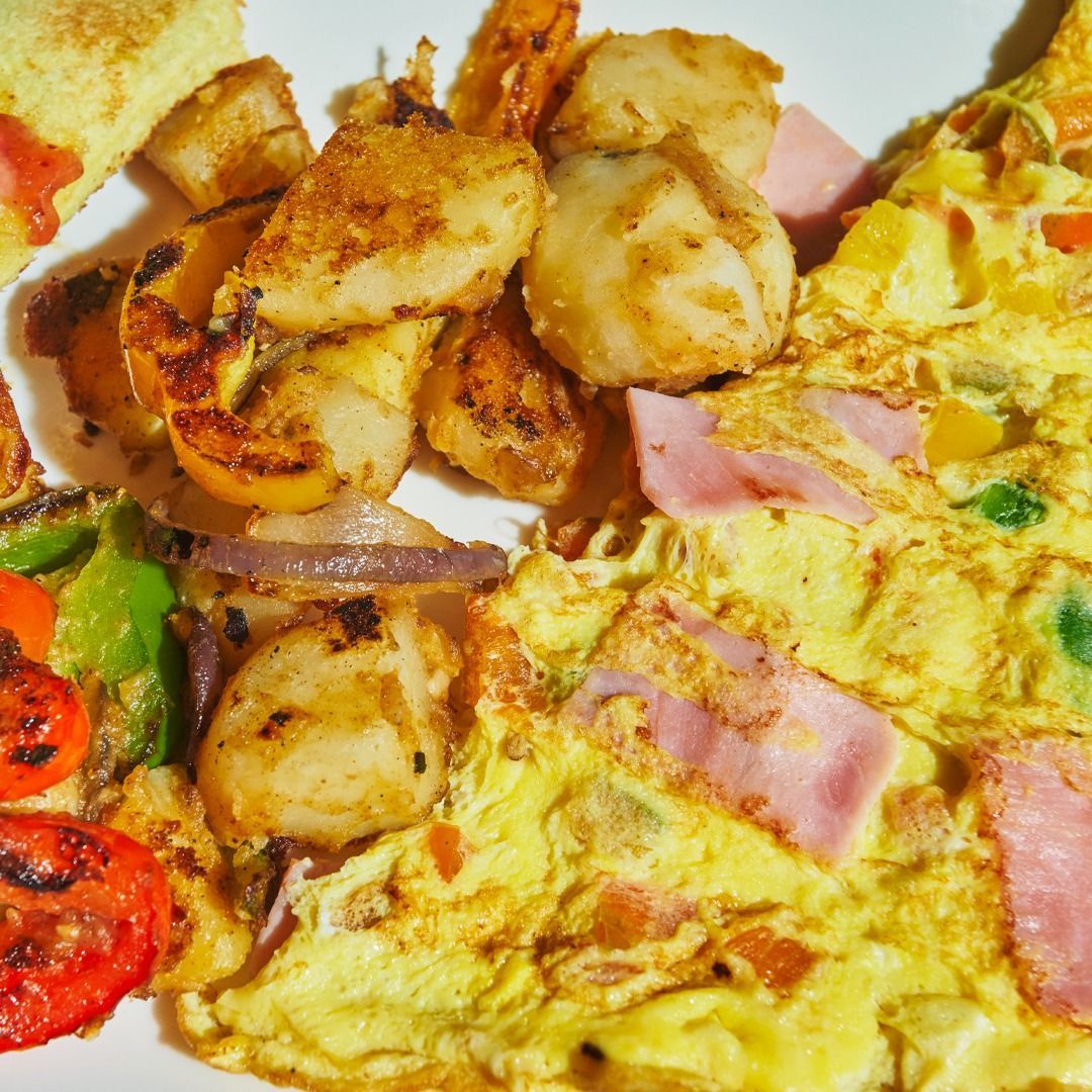 Breakfast plate with omelet, potatoes, ham, and vegetables.