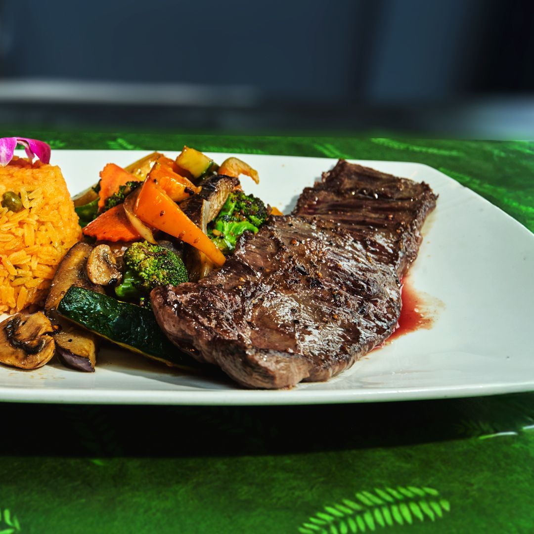 Steak with grilled vegetables and rice on a white plate.