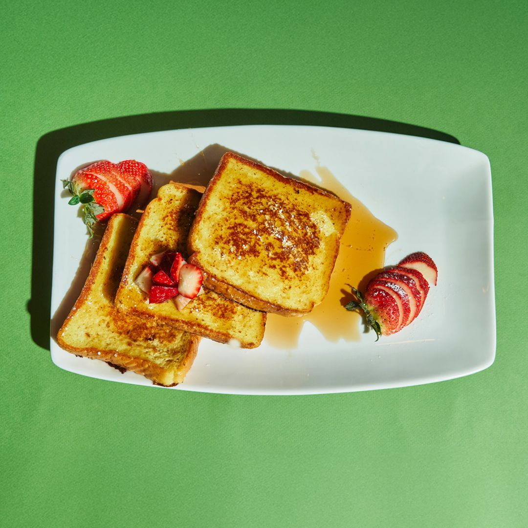 French toast with strawberries and syrup on a white plate, green background.