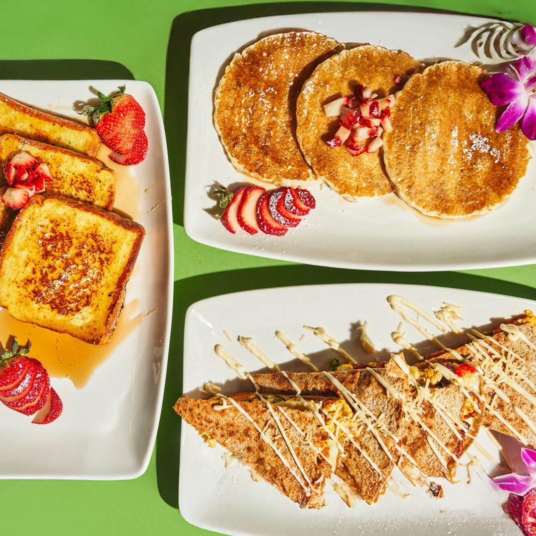Plates of breakfast food: French toast, pancakes, and a quesadilla, with strawberries and a green background.