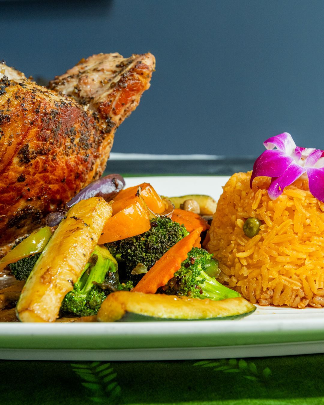 Roasted chicken, rice, and vegetables on a white plate. Includes a purple flower.
