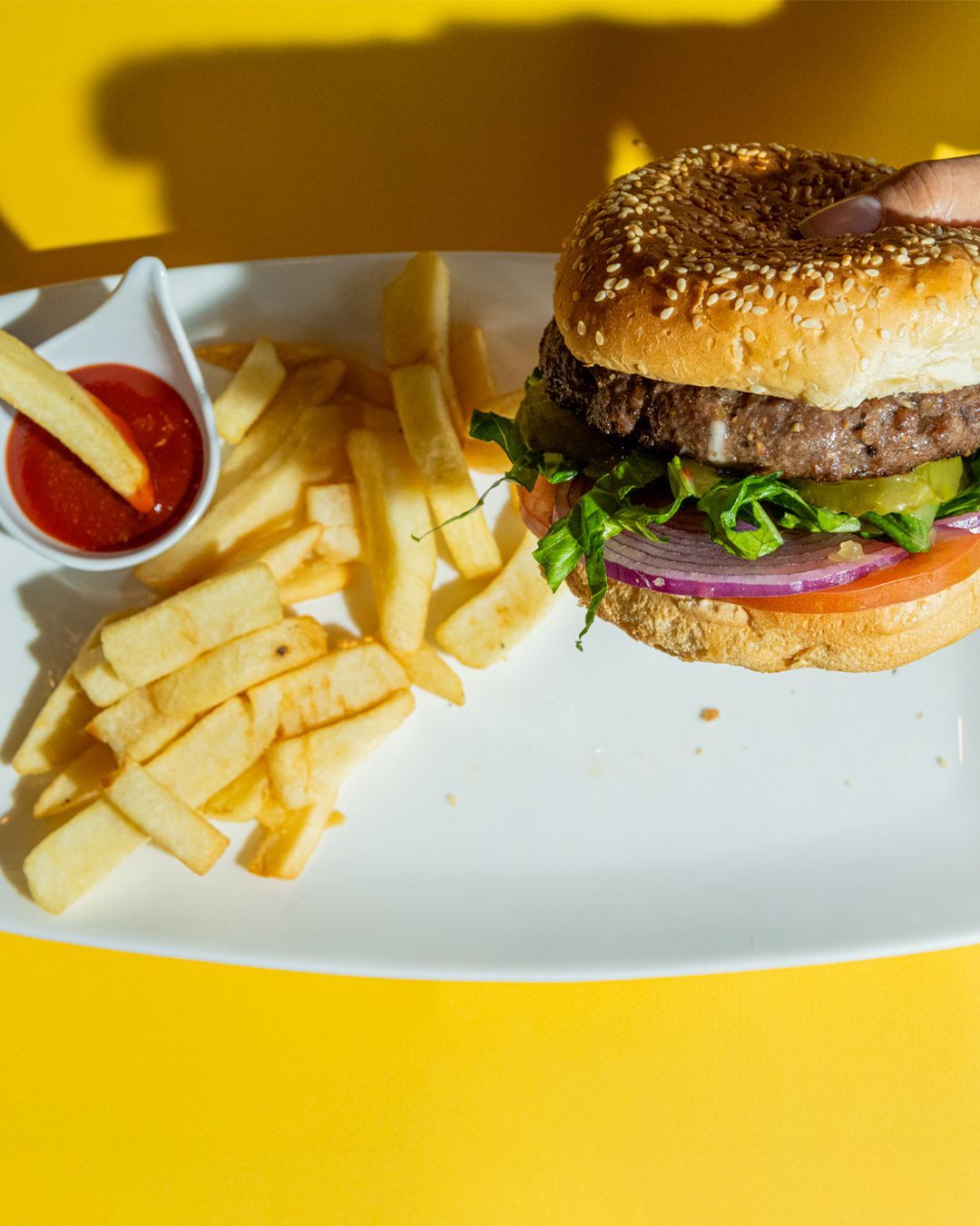 Burger on a plate with fries and ketchup. Yellow background.