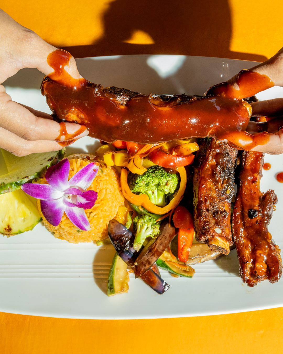 Plate of barbecued ribs with vegetables and someone holding a rib.