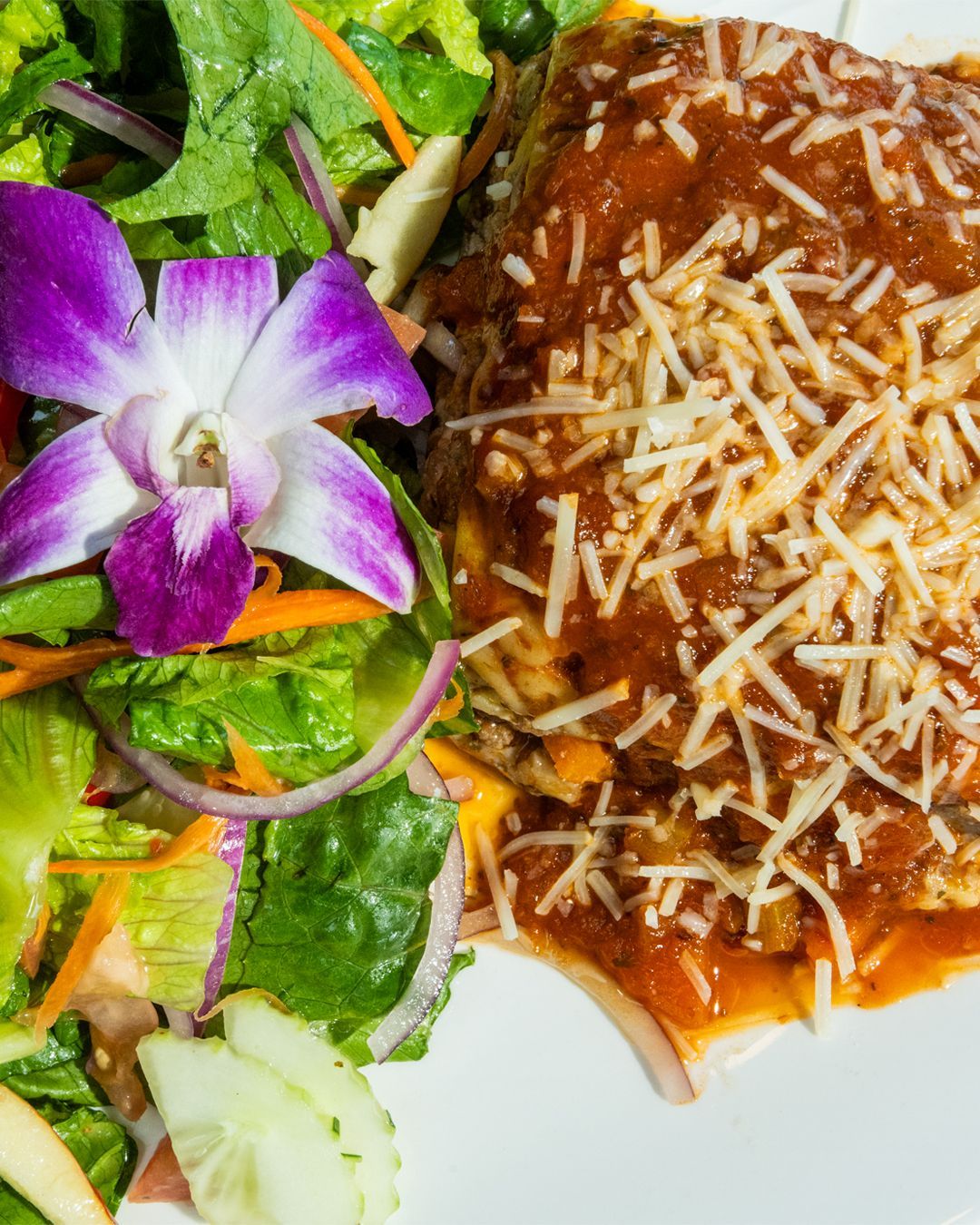 Lasagna with red sauce and grated cheese, served with a salad and purple orchid.