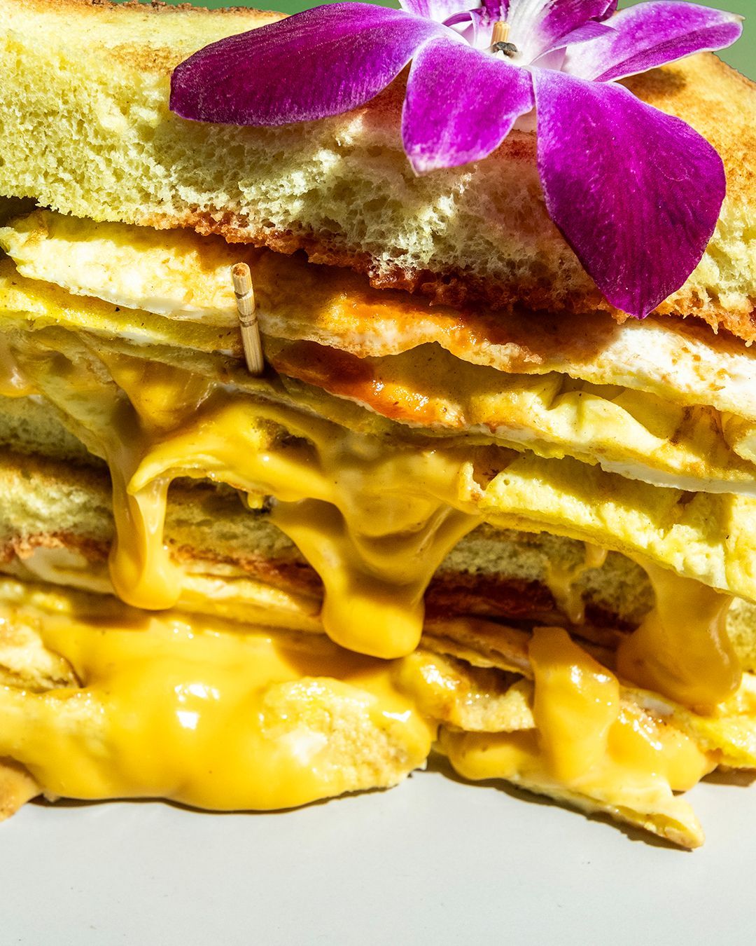 Grilled cheese sandwich with melted cheese dripping down, topped with a purple flower.