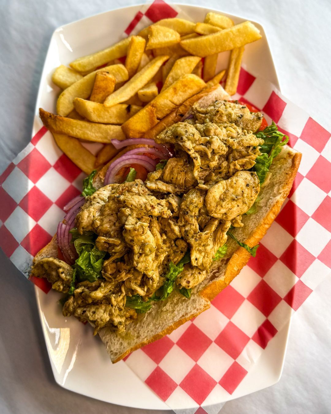 Chicken sandwich with fries on a red-checkered plate.