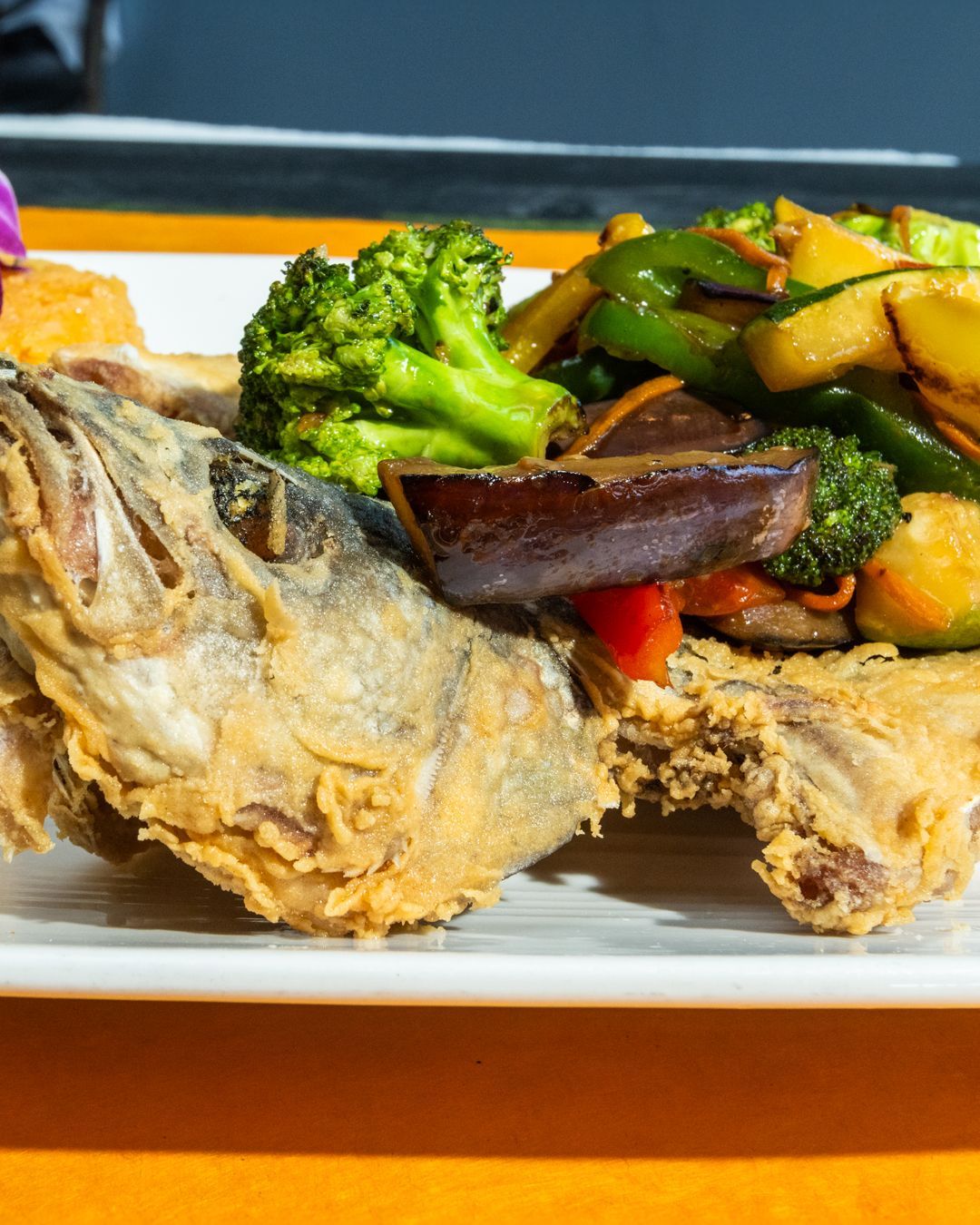 Fried whole fish with broccoli and stir-fried vegetables on a white plate.