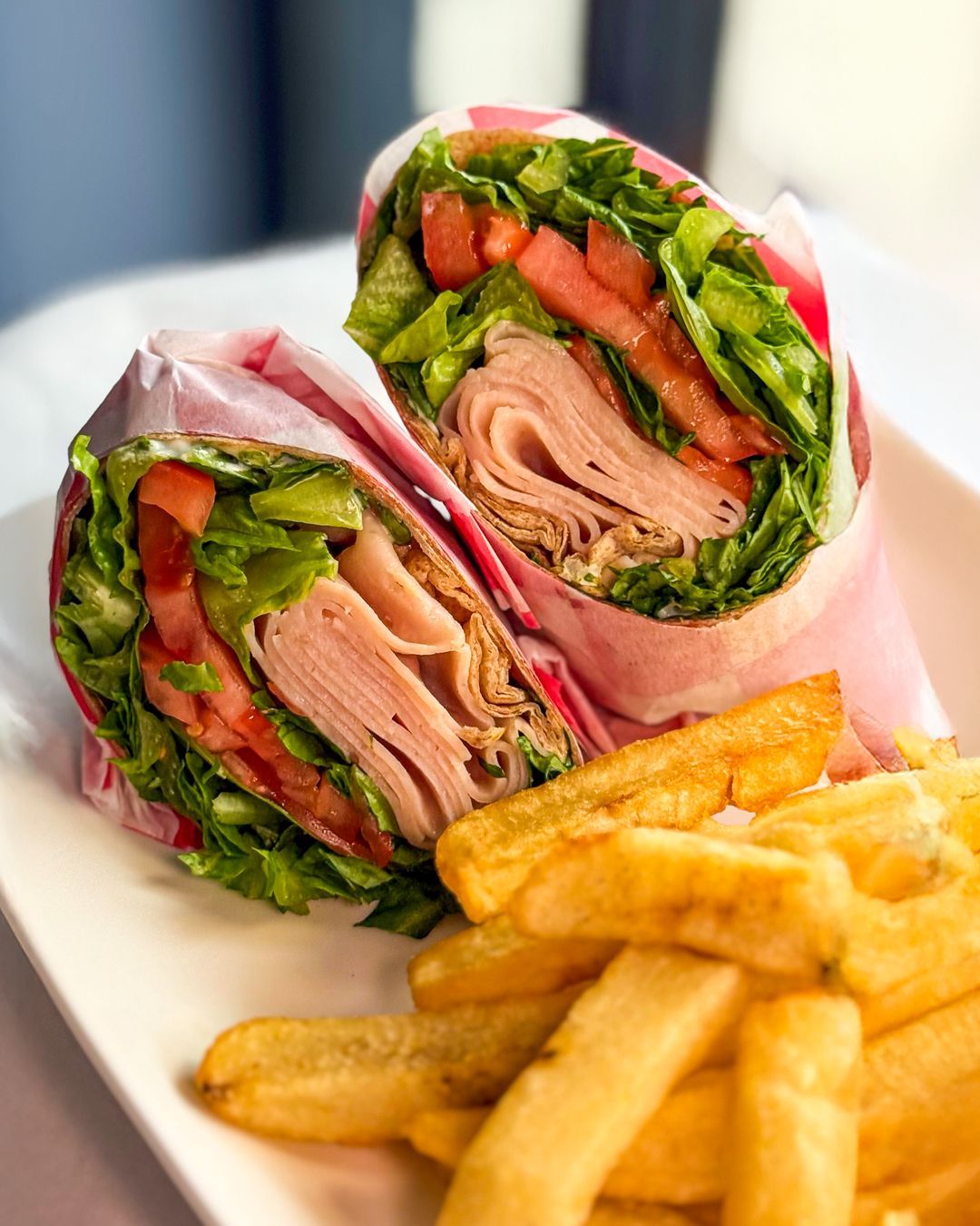 Wrap sandwich cut in half, filled with turkey, lettuce, and tomato, served with french fries on a white plate.