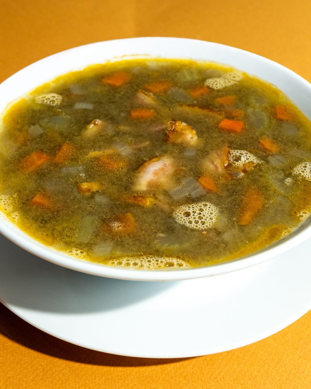 Bowl of soup with visible vegetables and meat in a white bowl on an orange surface.