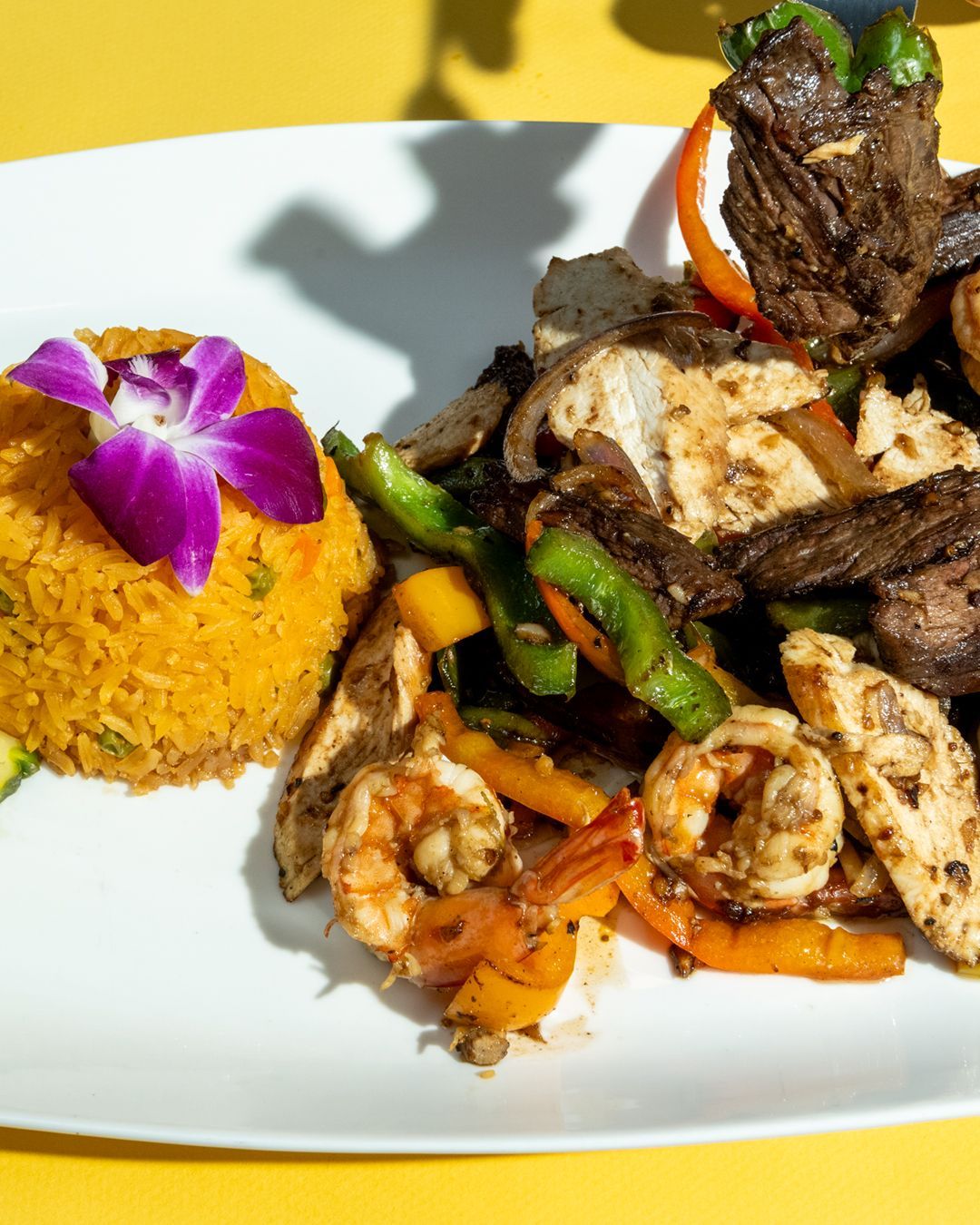 Plate with Mexican rice and mixed grilled meats and shrimp, garnished with flower.