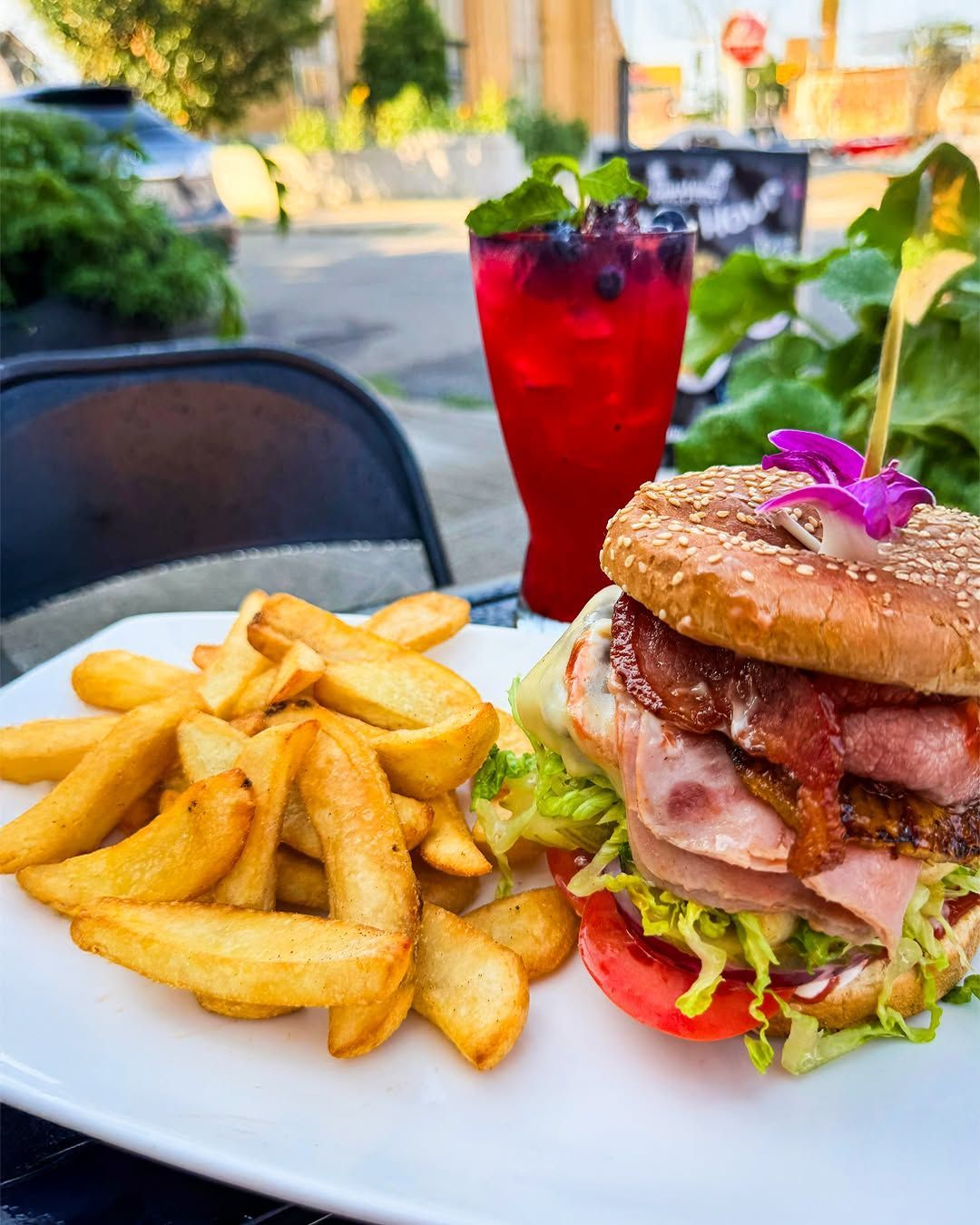 Plate with burger, fries, and red drink with mint, outdoor seating.