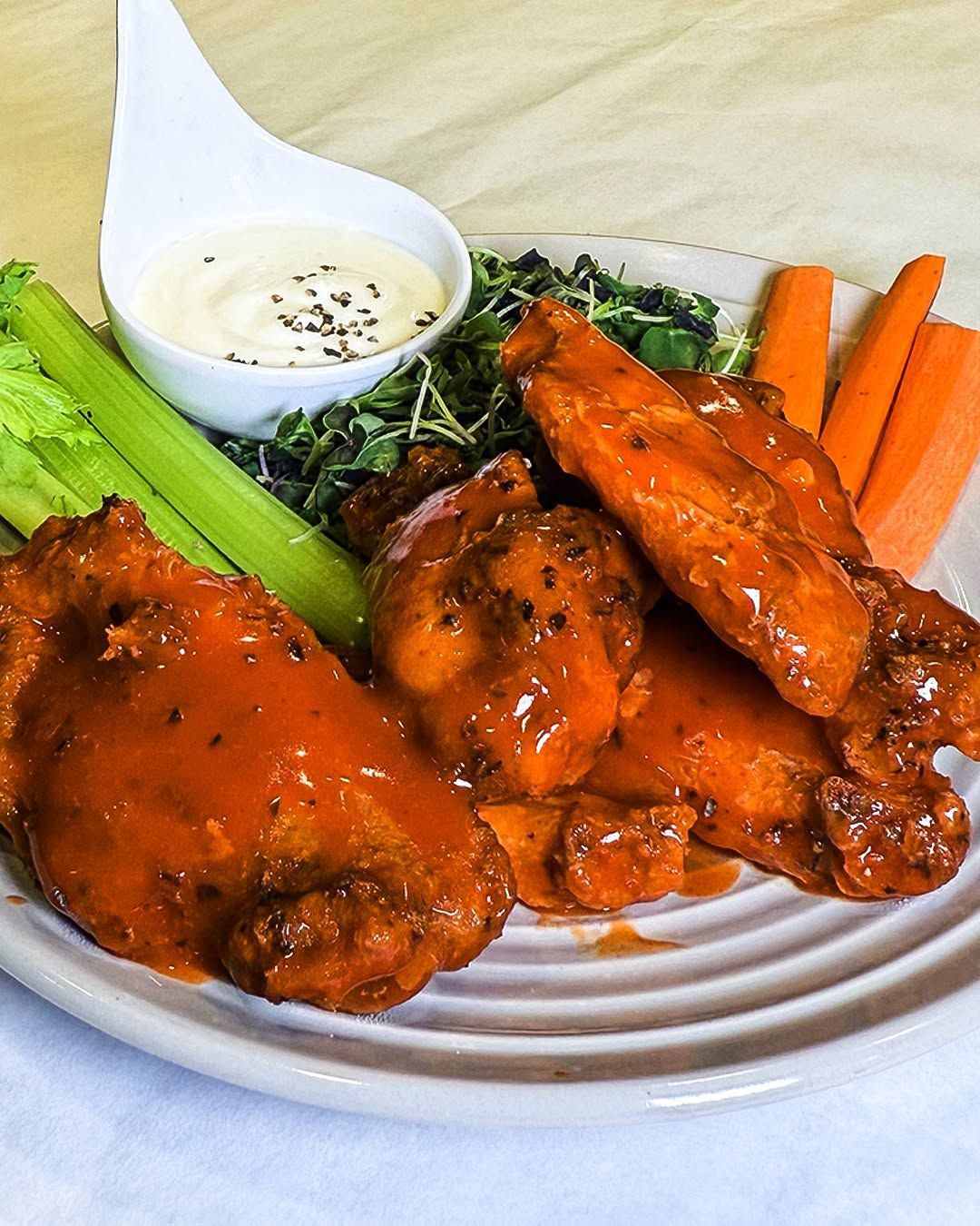 Buffalo wings with dip, celery, and carrots on a plate.