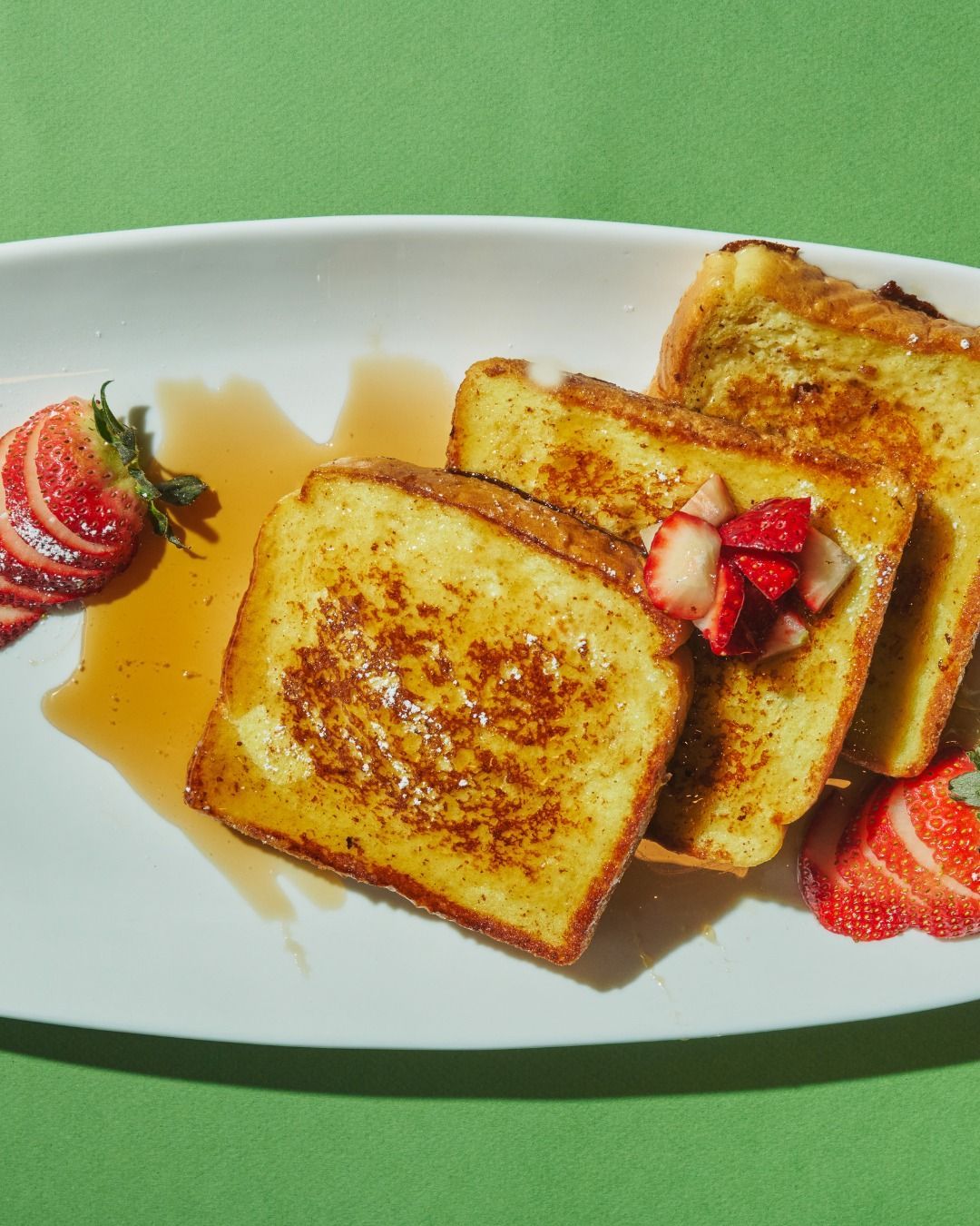 French toast with strawberries and syrup on a white plate, green background.