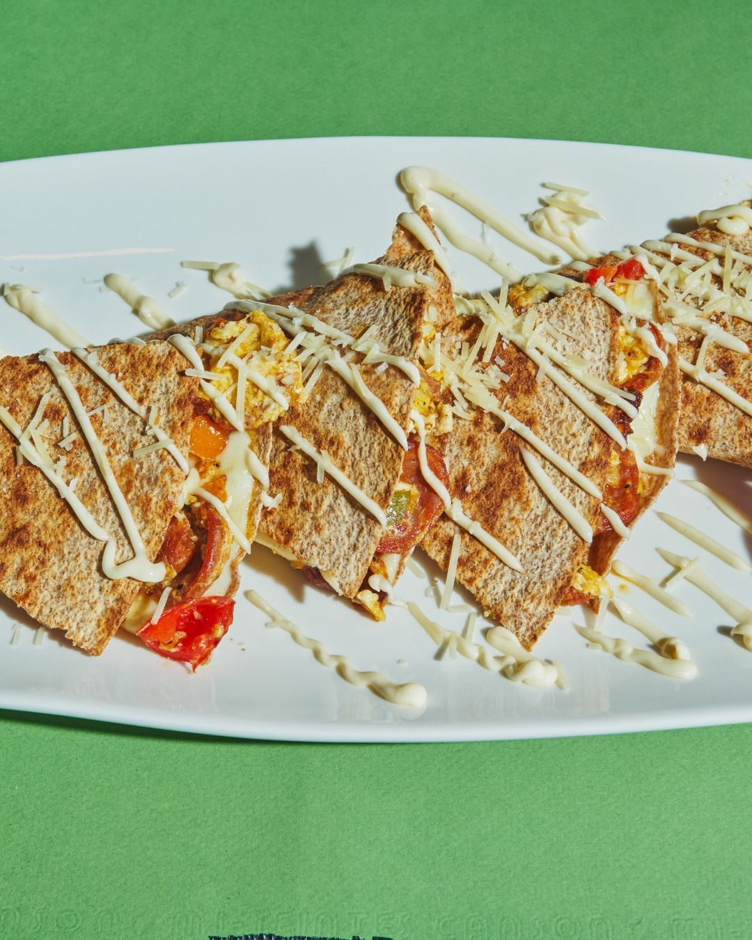 Quesadillas with cheese and sauce drizzled on a white plate, green background.