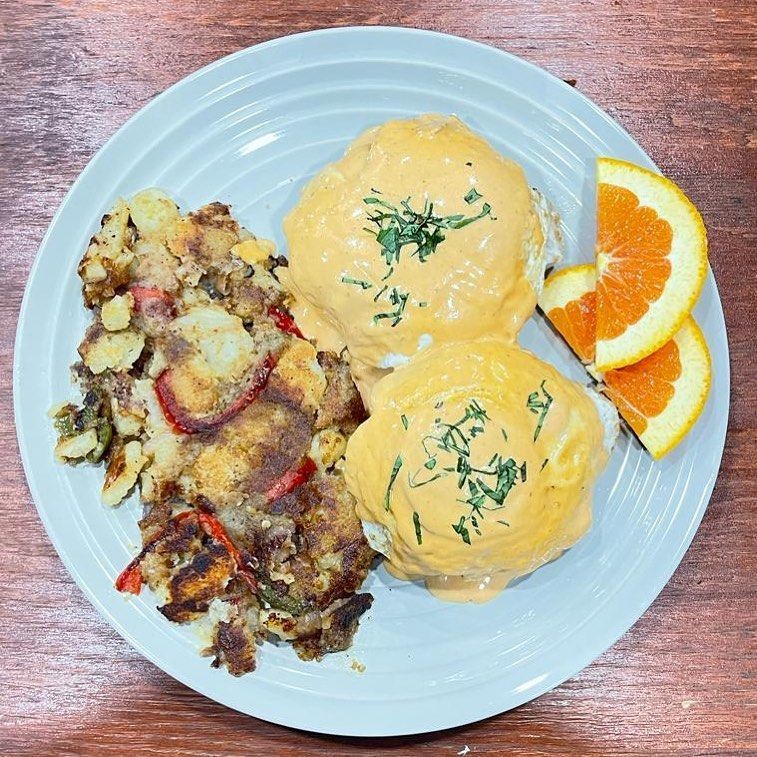 Eggs Benedict with potato hash and orange slices on a plate.