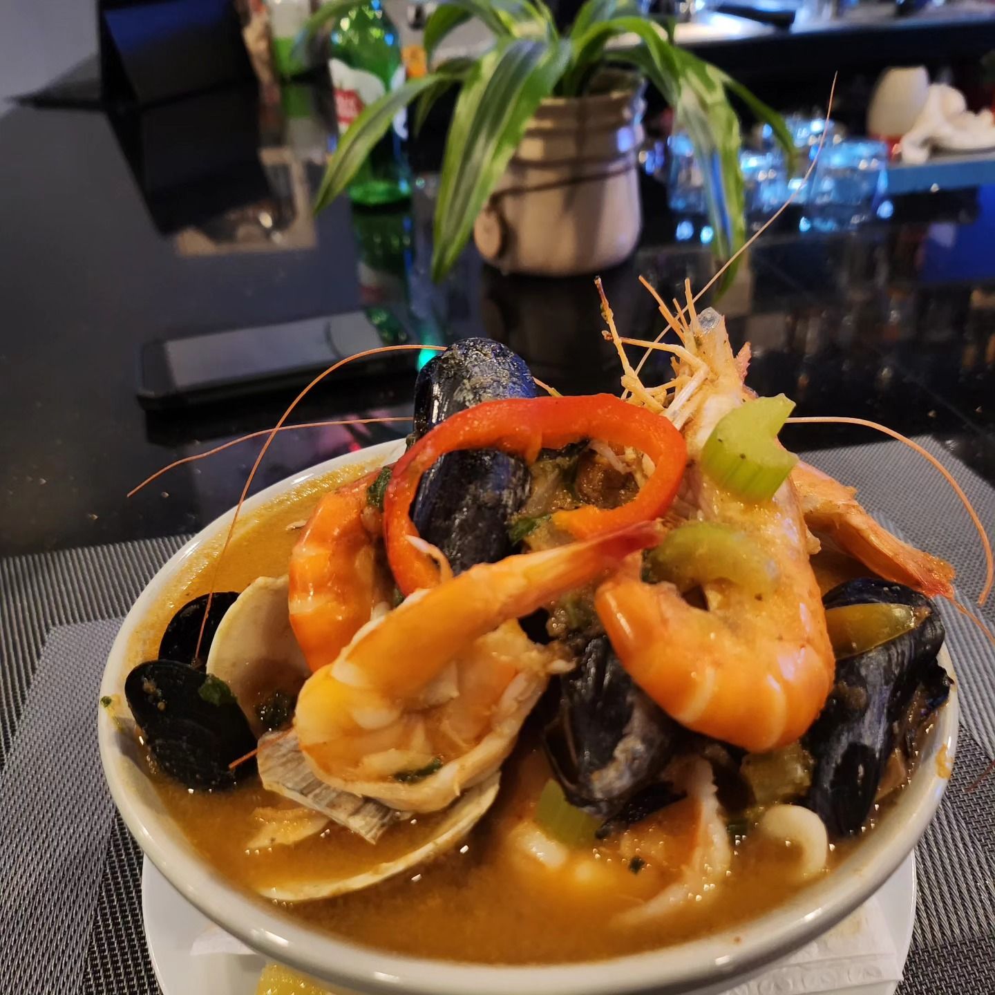 Seafood stew in a white bowl, with shrimp, mussels, clams, and red pepper ring.