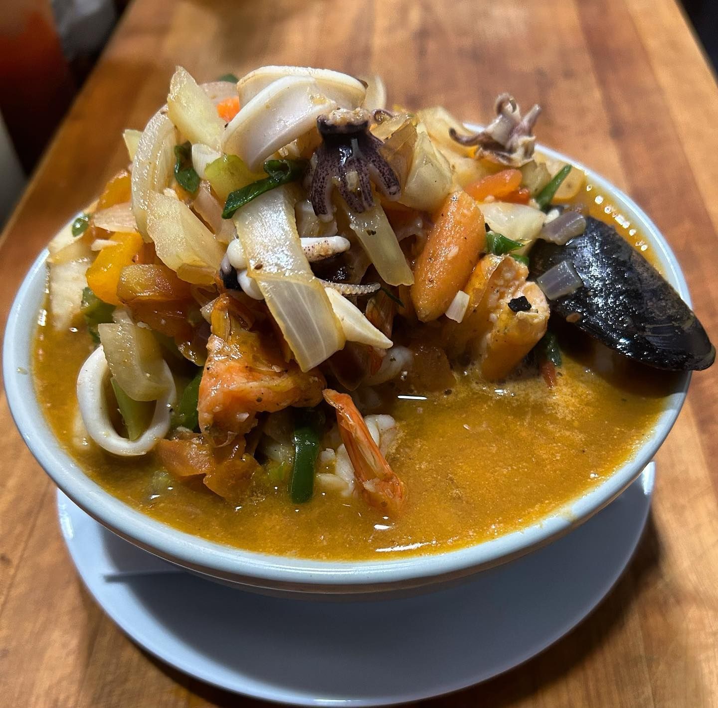 Bowl of seafood soup with squid, vegetables, and a mussel.