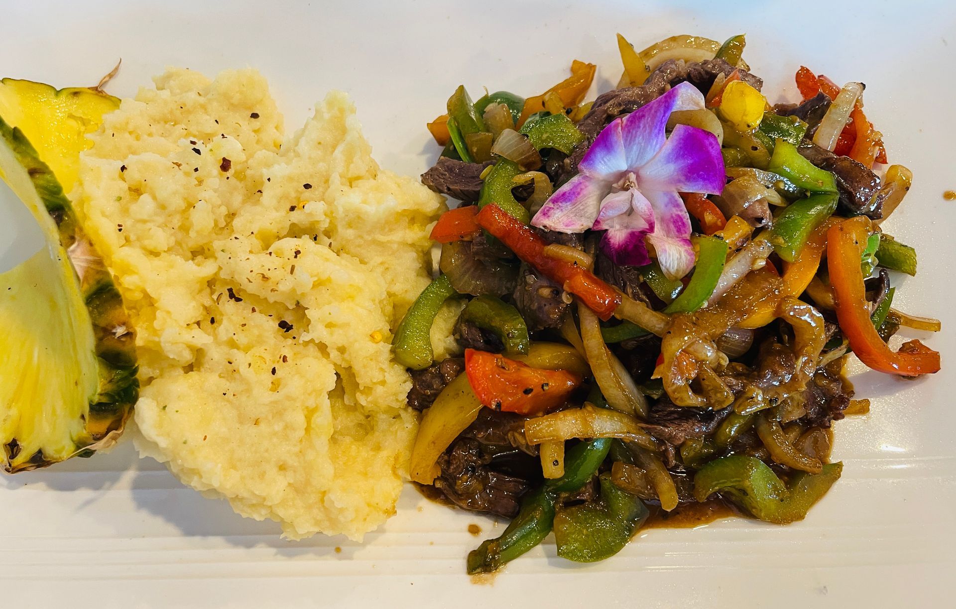 Beef stir-fry with bell peppers, onions, and fried rice, garnished with a flower and pineapple.