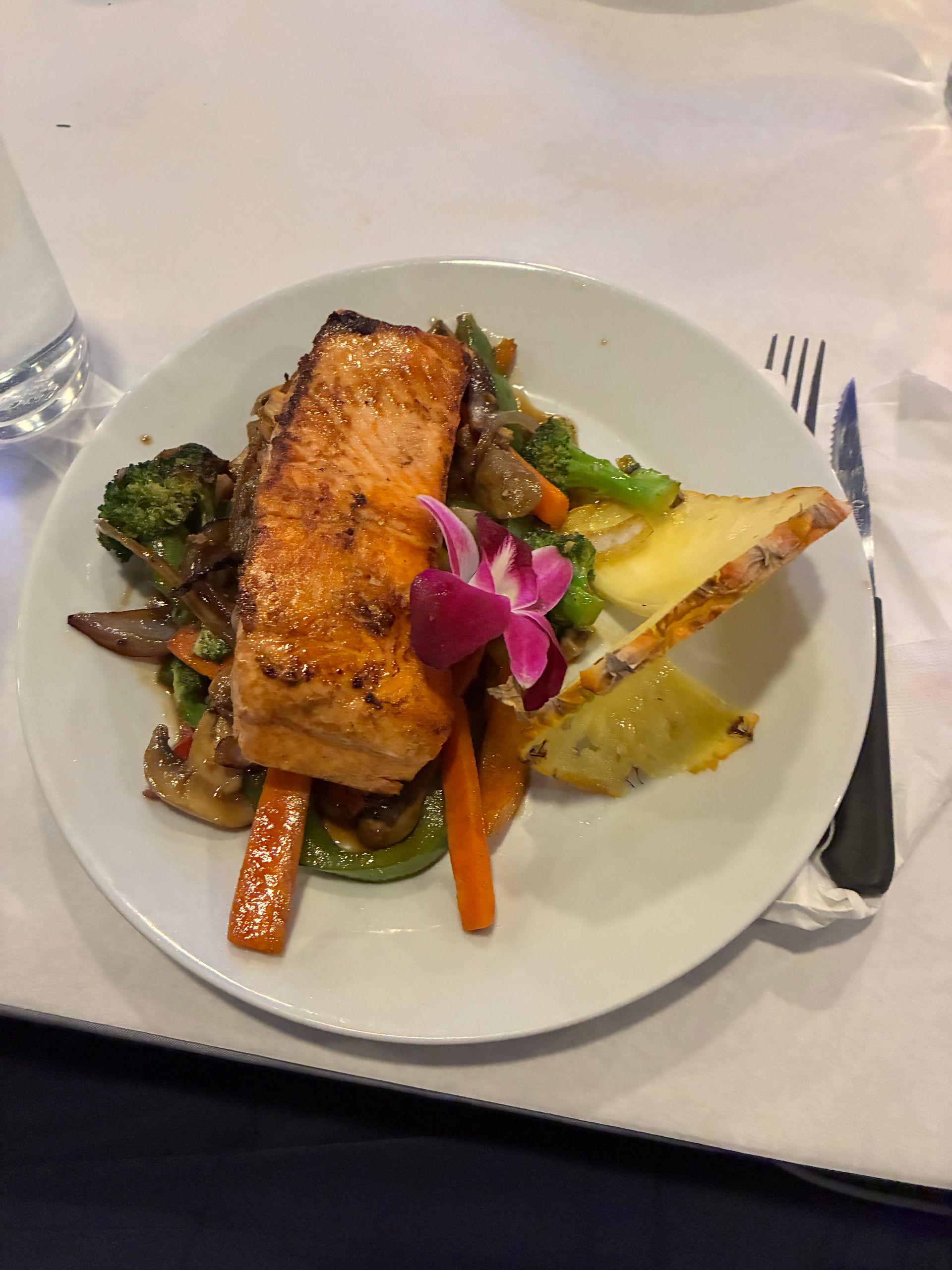 Grilled salmon with vegetables and pineapple on a white plate, with a fork and knife.