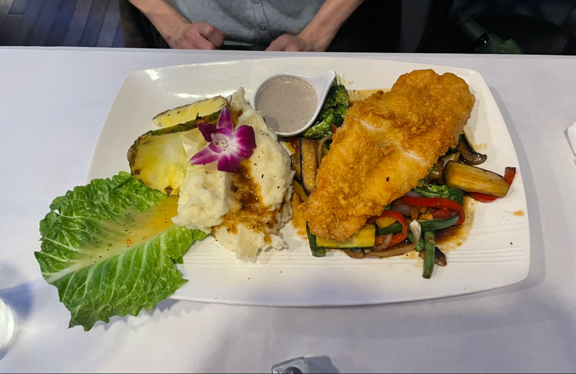 Plate of food: breaded fish, mashed potatoes, vegetables, pineapple, and gravy.